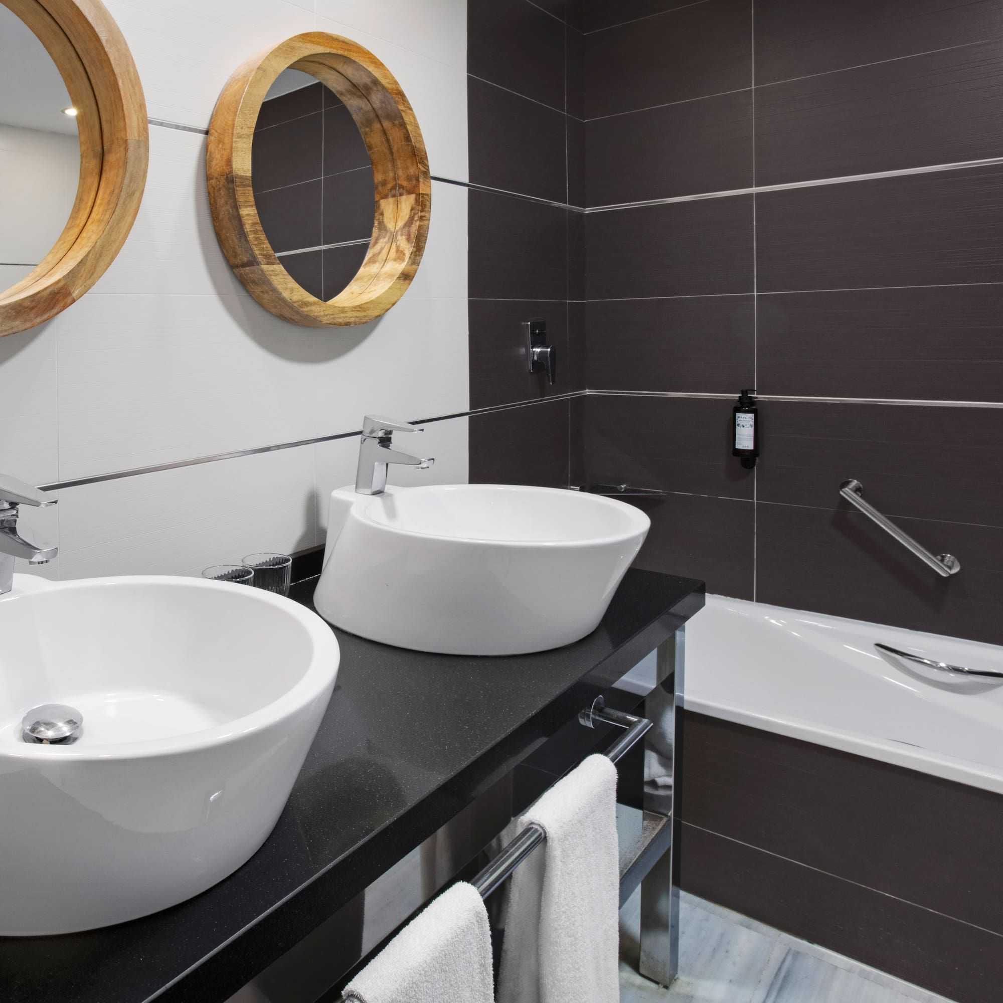 Modern bathroom with two vessel sinks, round wooden mirrors, and bathtub.