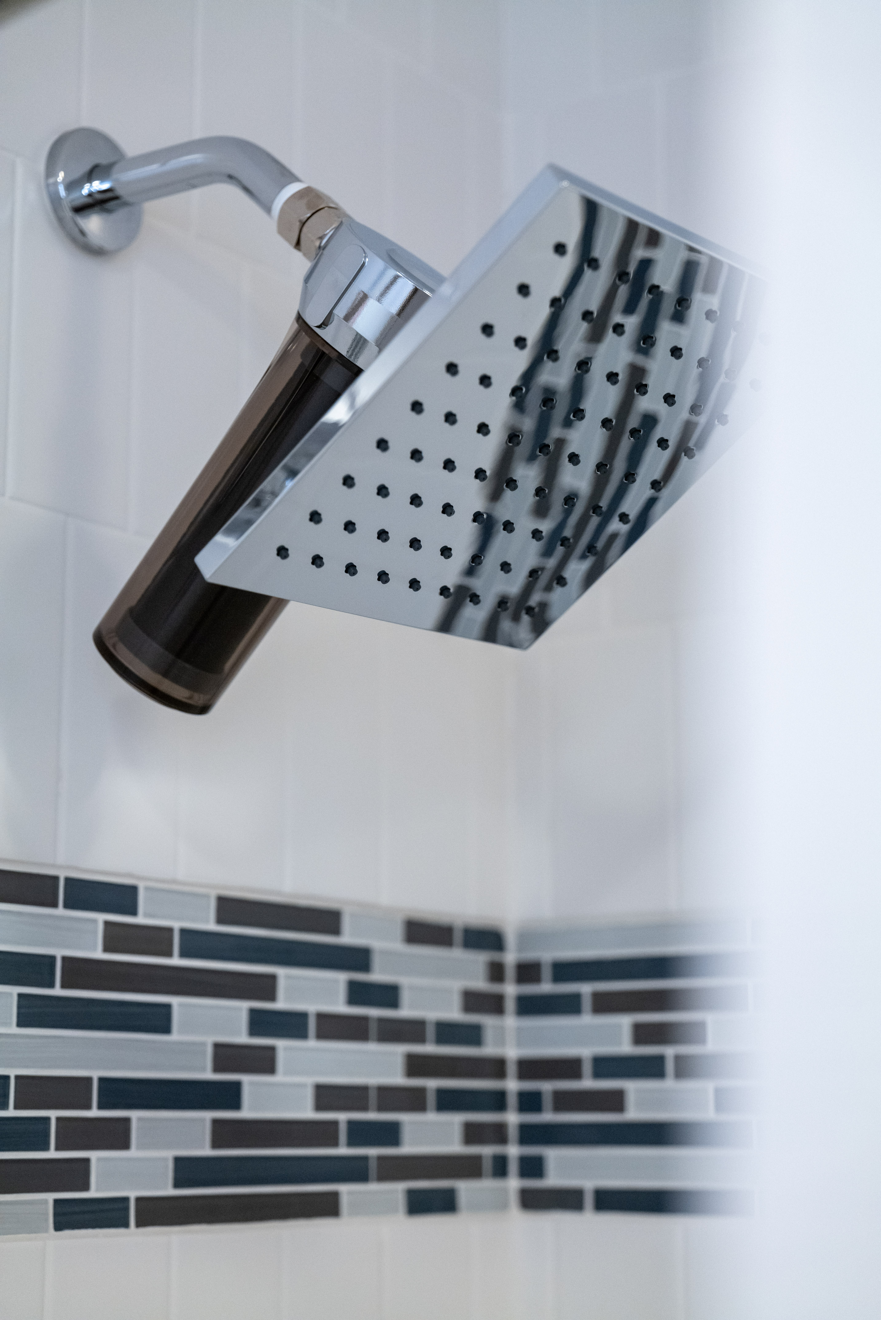 Modern square chrome shower head with filter and blue mosaic tile accent.