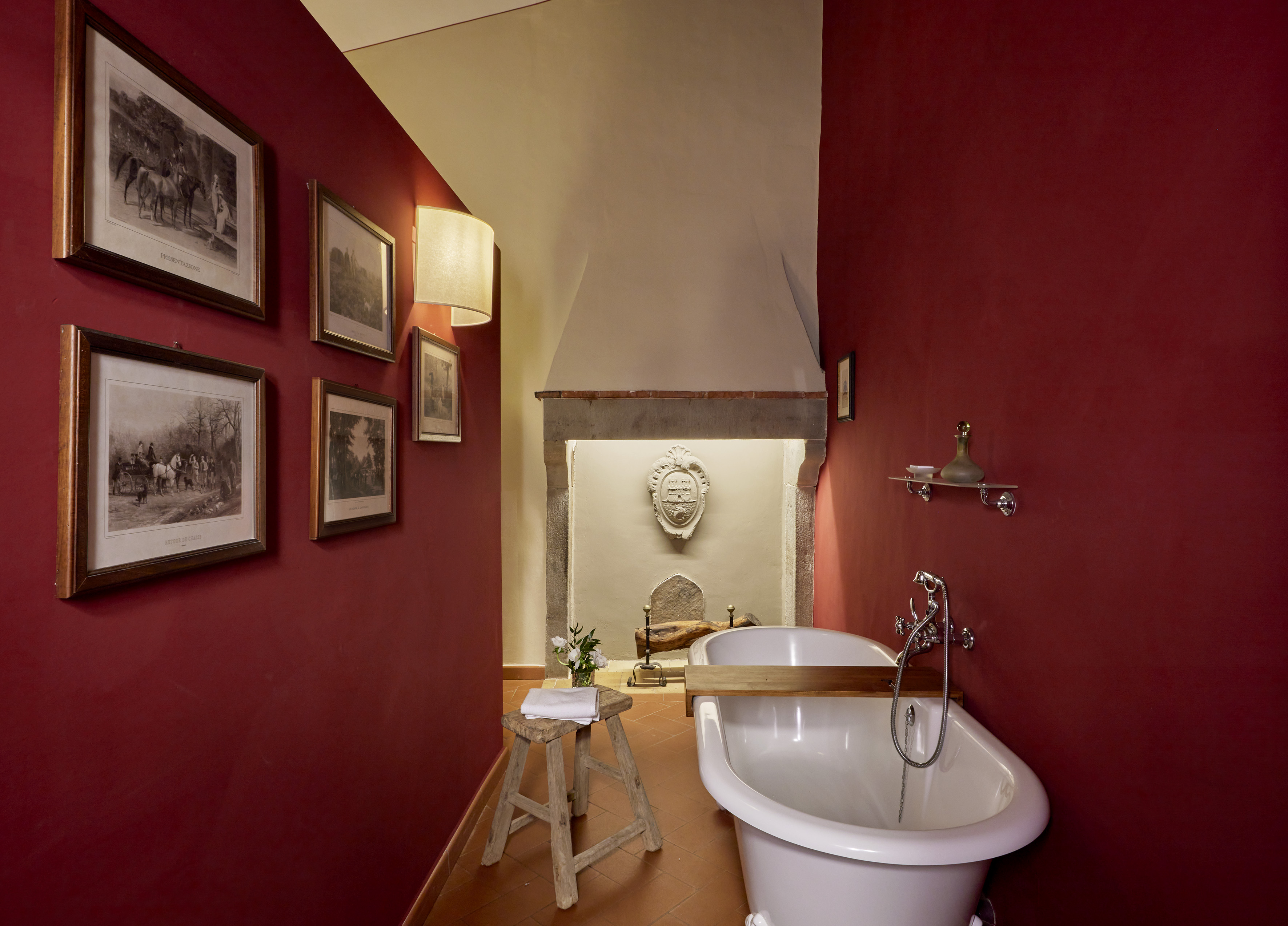 Rustic red bathroom with freestanding tub, stone fireplace, and framed art.