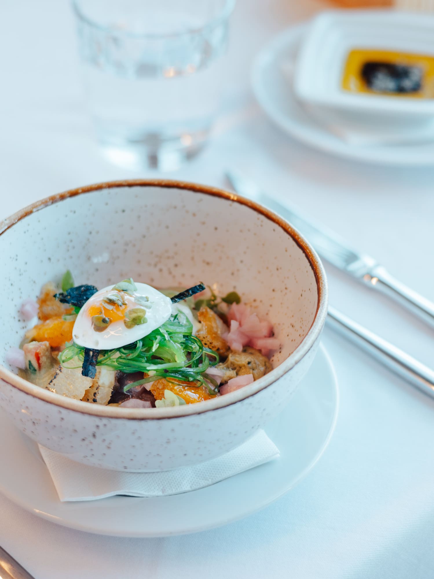 Fresh poké bowl with soft egg, seaweed, and vibrant toppings on a white table.