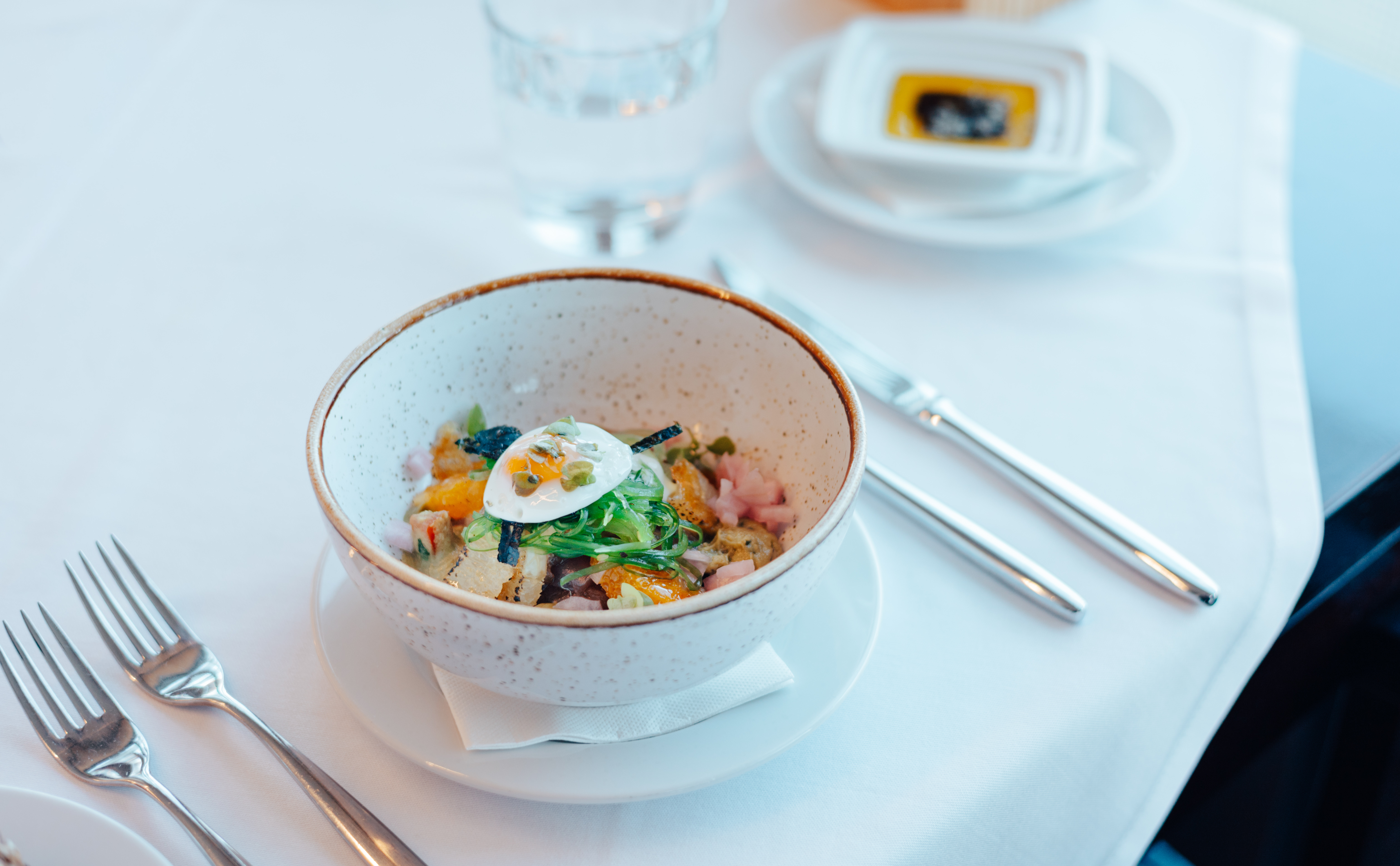 Fresh poké bowl with soft egg, seaweed, and vibrant toppings on a white table.