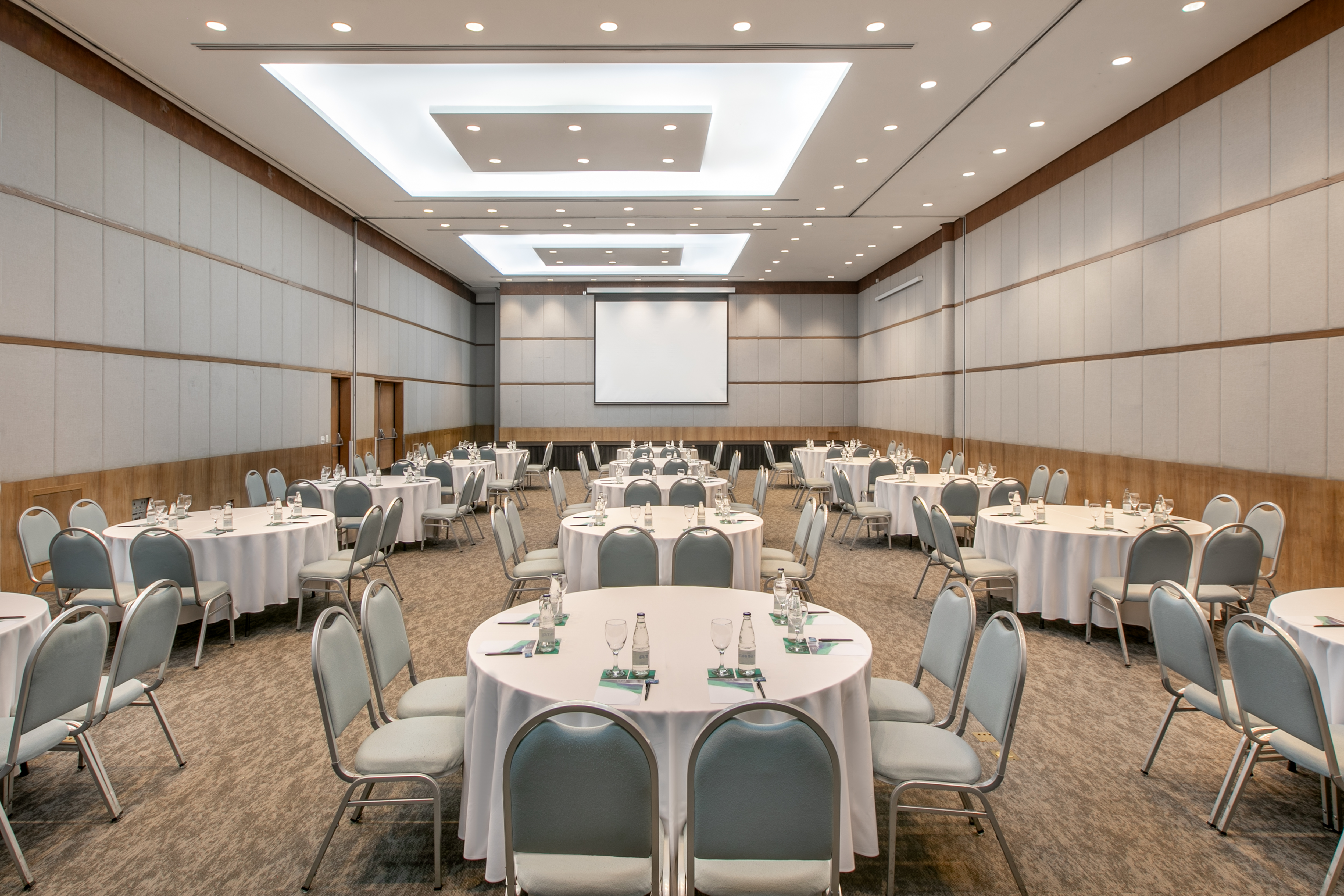 Modern conference room with tables, chairs, projector screen for events.