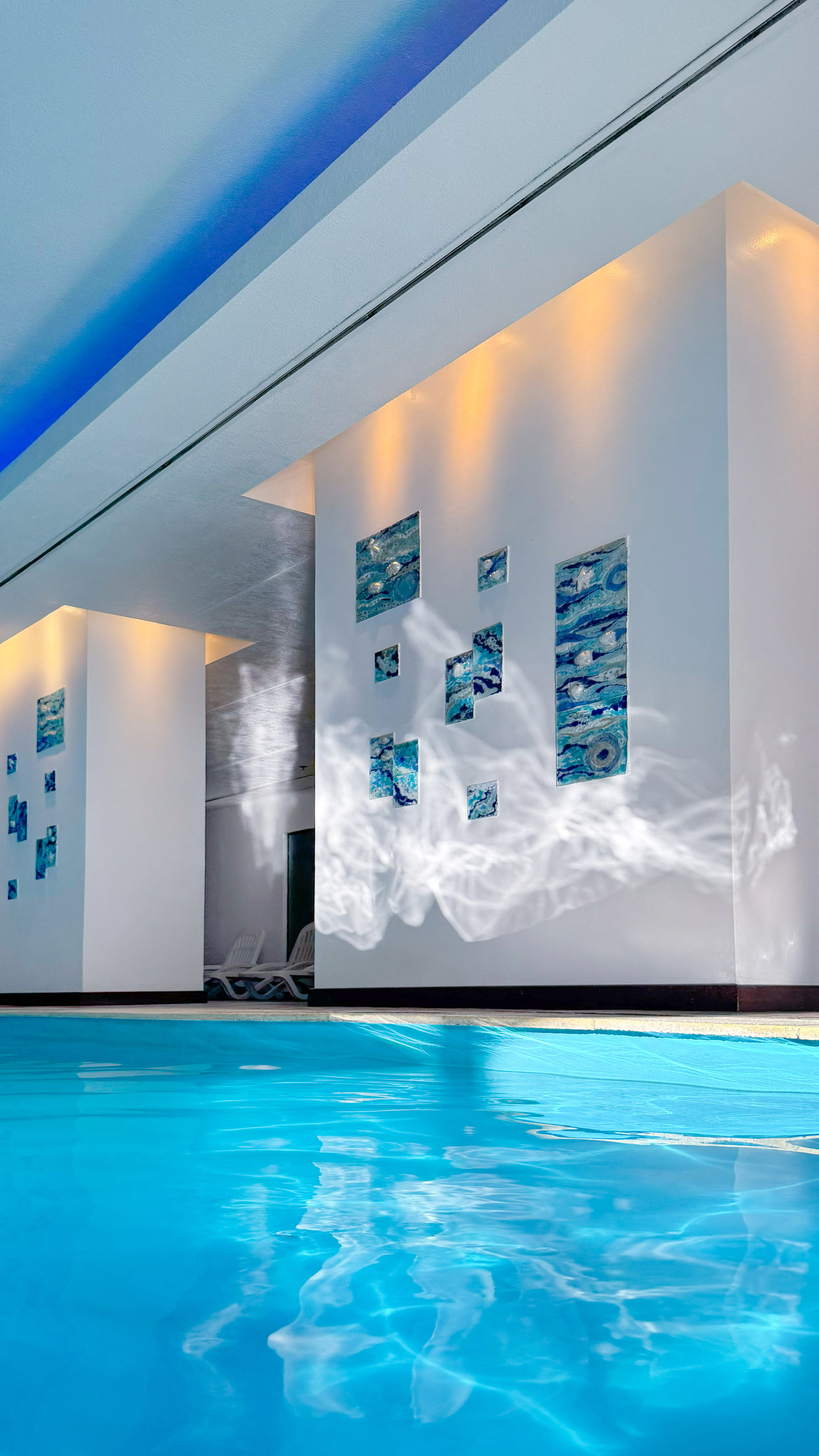 Indoor pool with blue water, abstract art on walls, and light reflections.