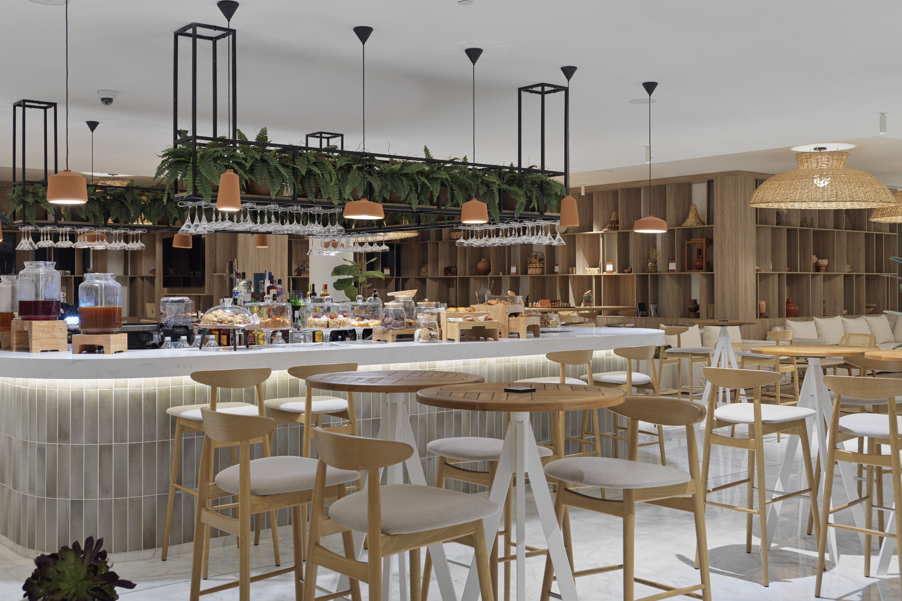 Modern hotel bar with buffet counter, hanging plants, and wooden stools.