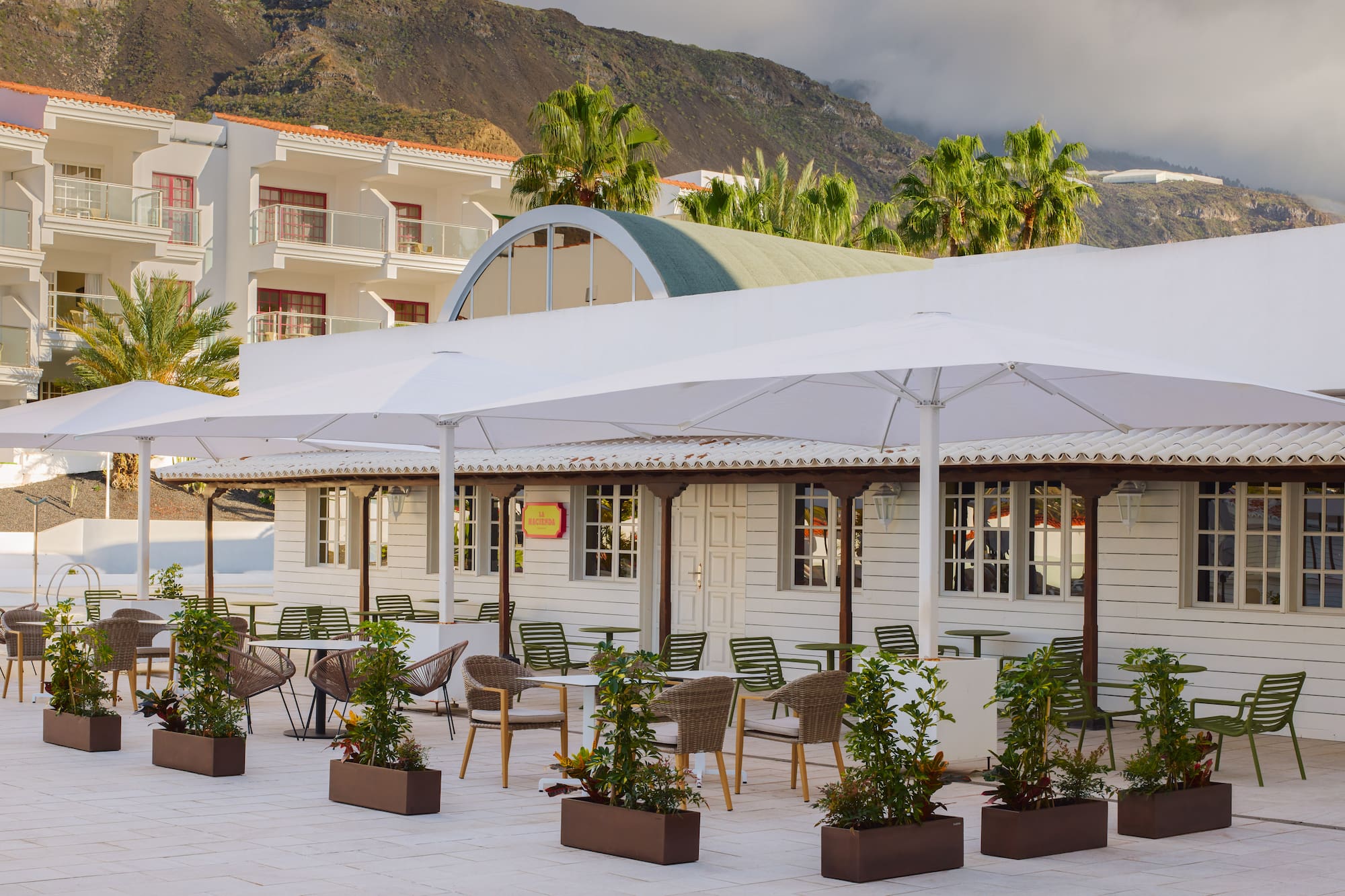 Outdoor resort dining terrace with white umbrellas, hotel, mountain view.