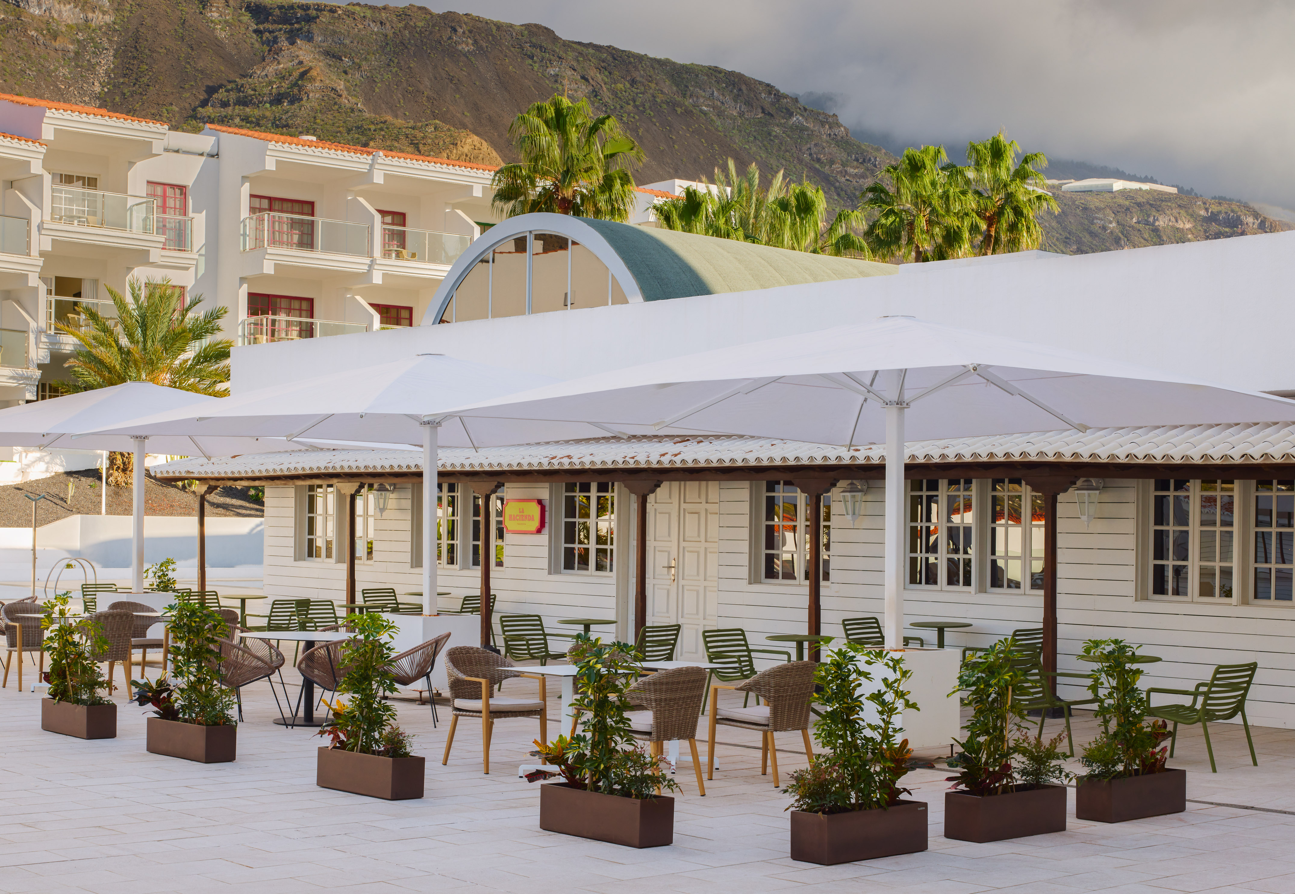 Outdoor resort dining terrace with white umbrellas, hotel, mountain view.