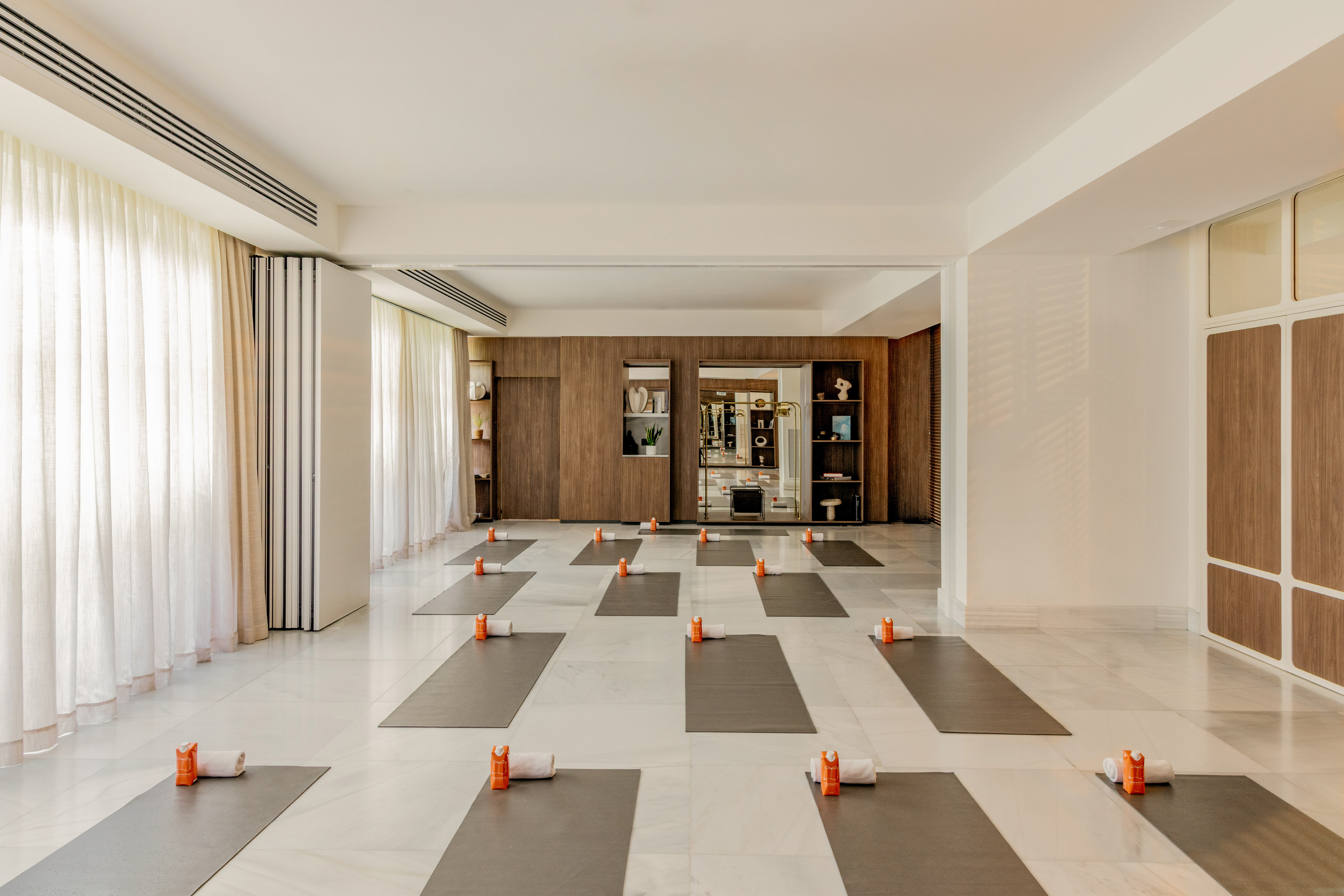 Bright yoga studio with mats, towels, and orange bottles on marble.