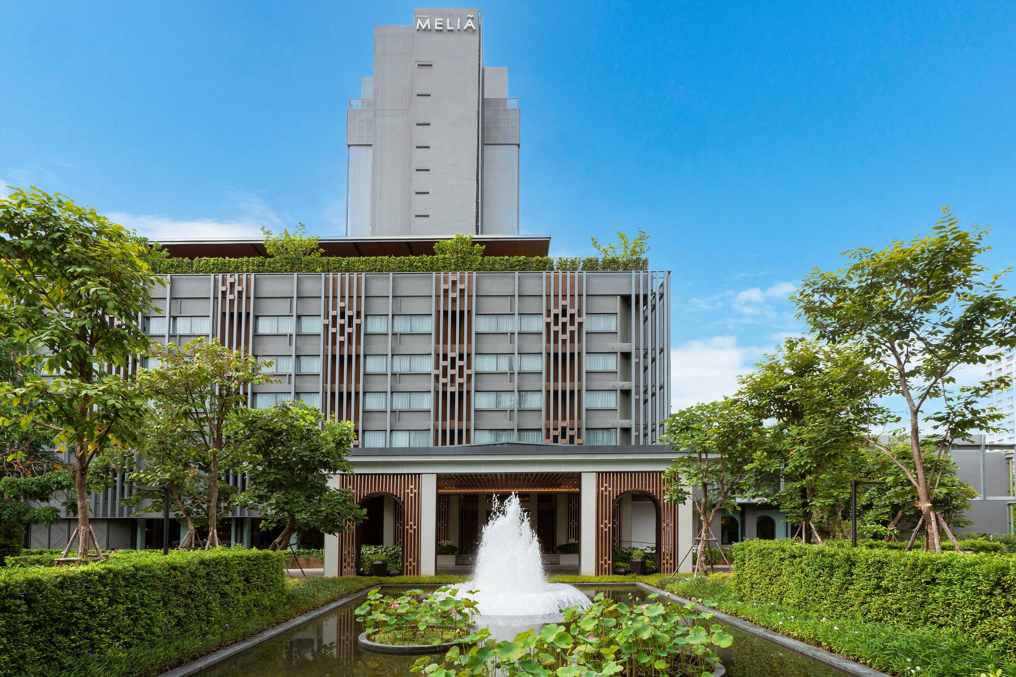 Meliá hotel with modern grey facade, green landscaping, and fountain.