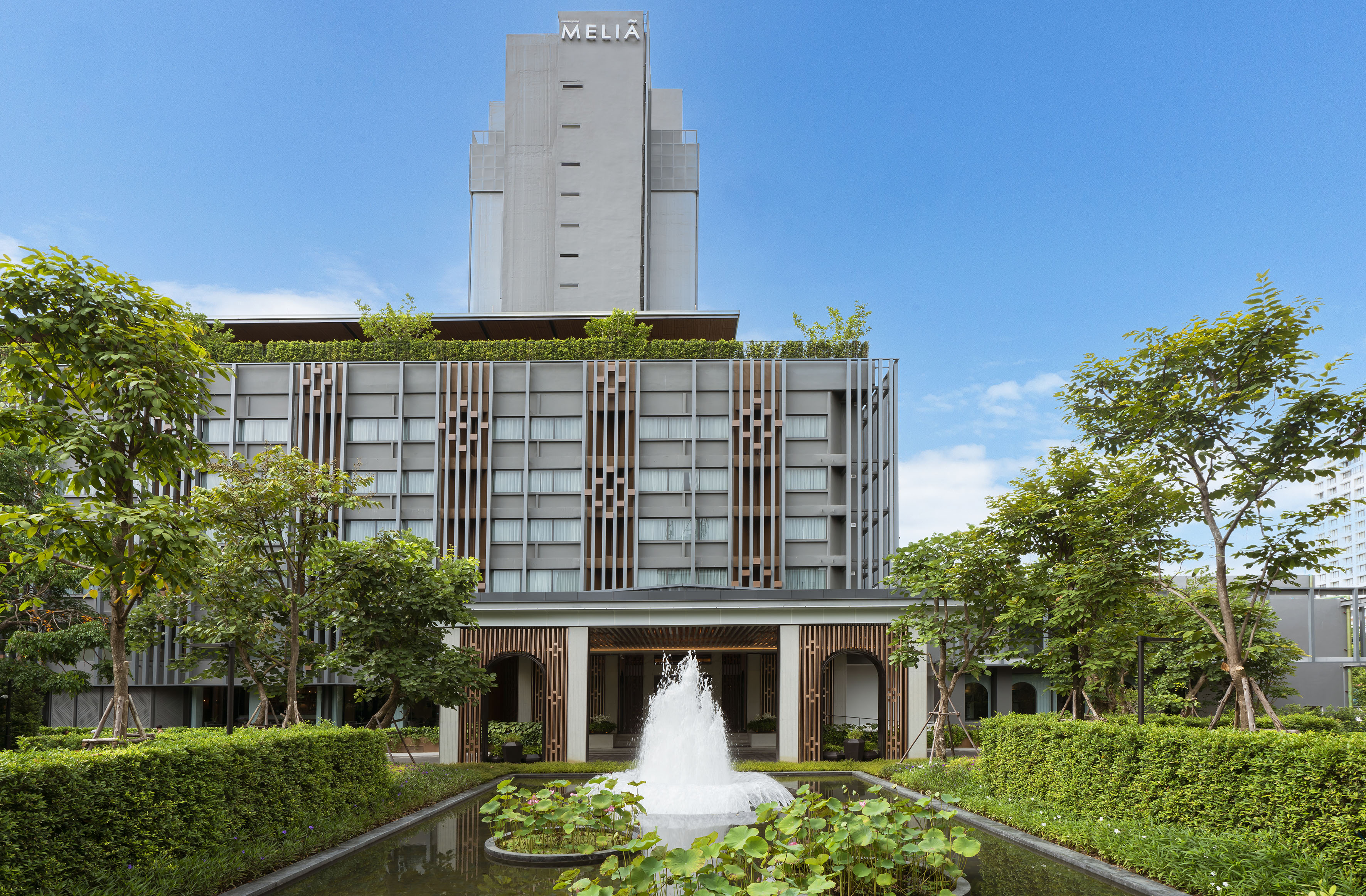Meliá hotel with modern grey facade, green landscaping, and fountain.