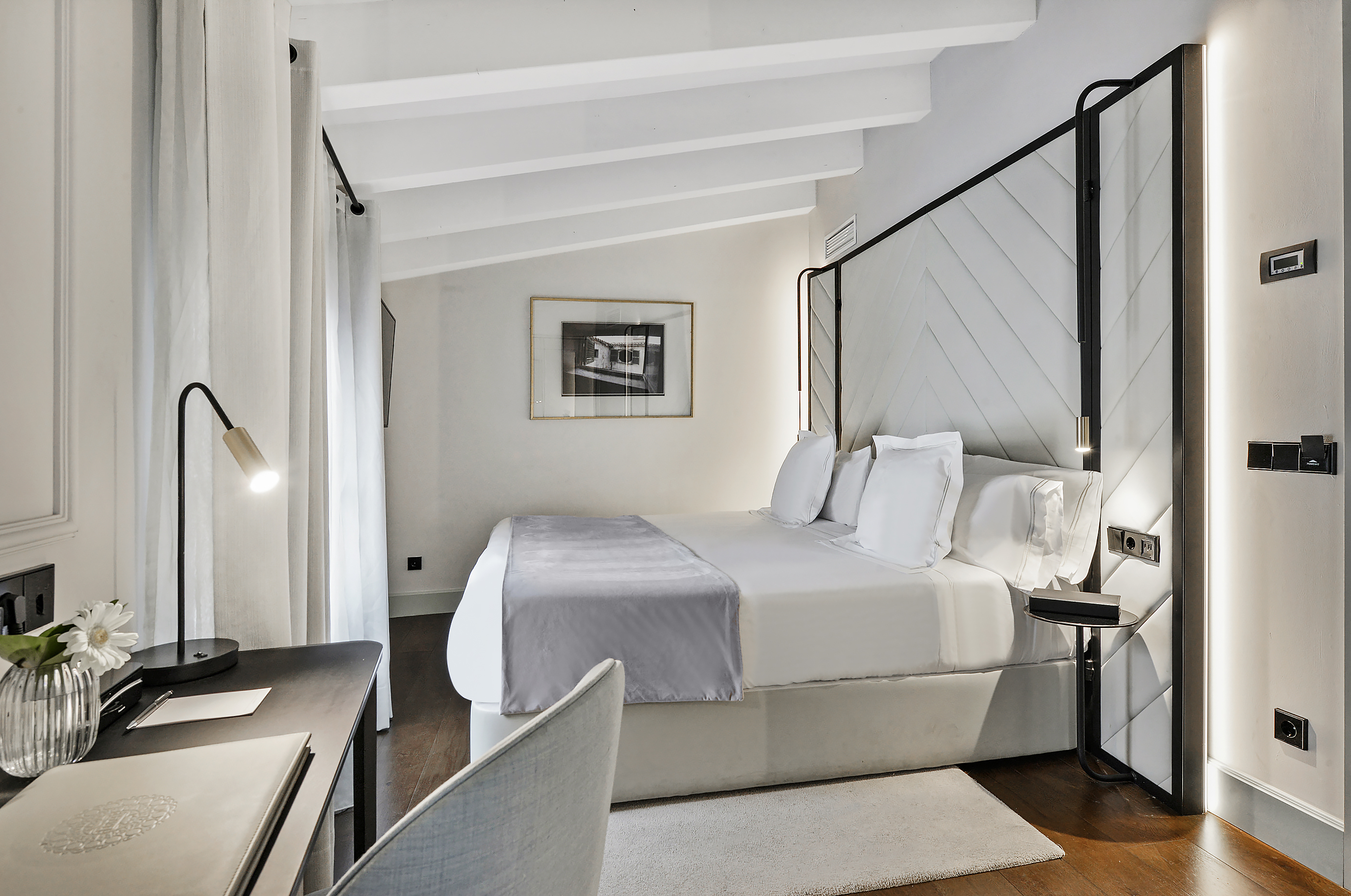 Stylish hotel bedroom with a white bed, patterned headboard, and desk area.