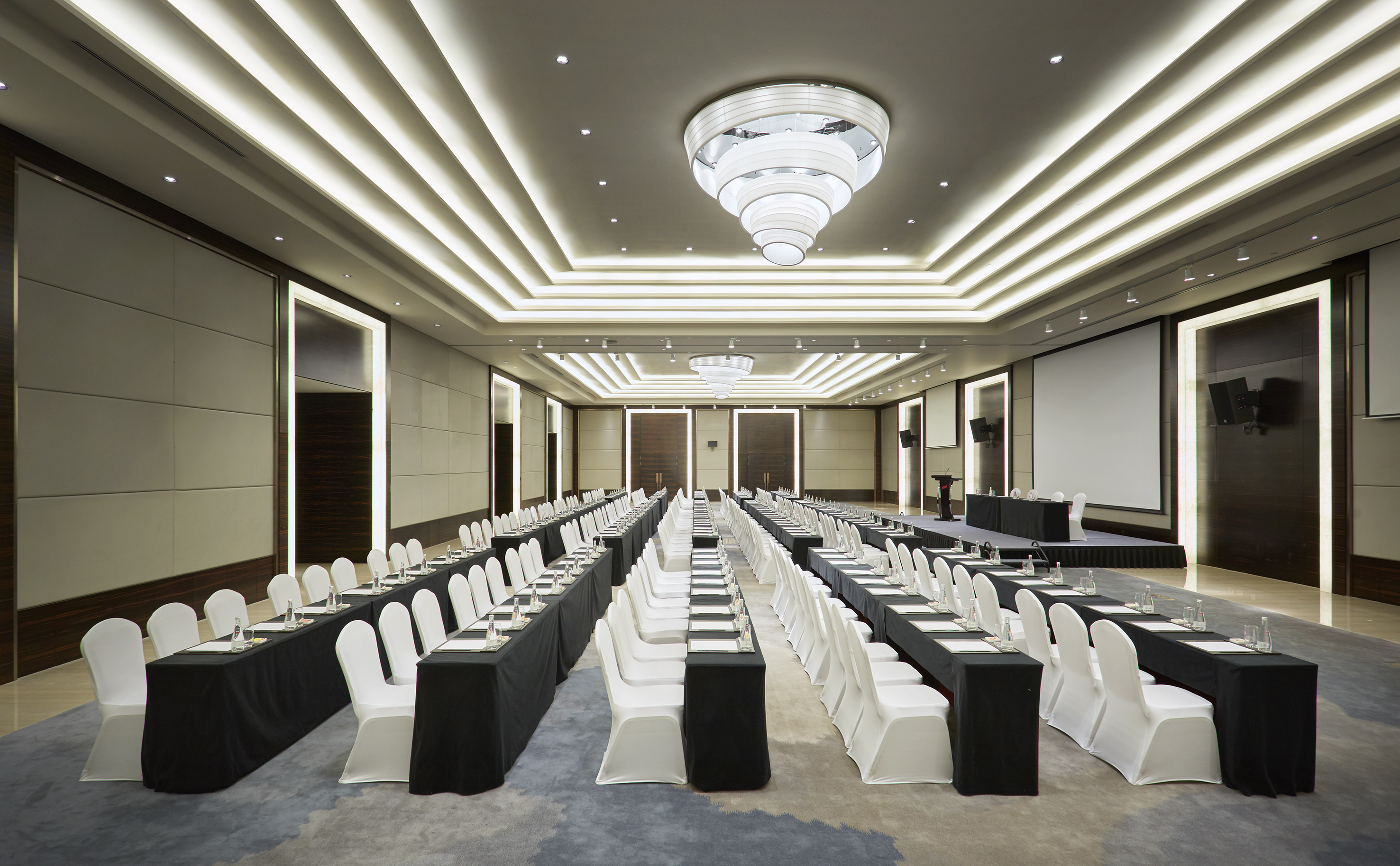 Meeting room with classroom setup, white chairs, tables, projection screens.