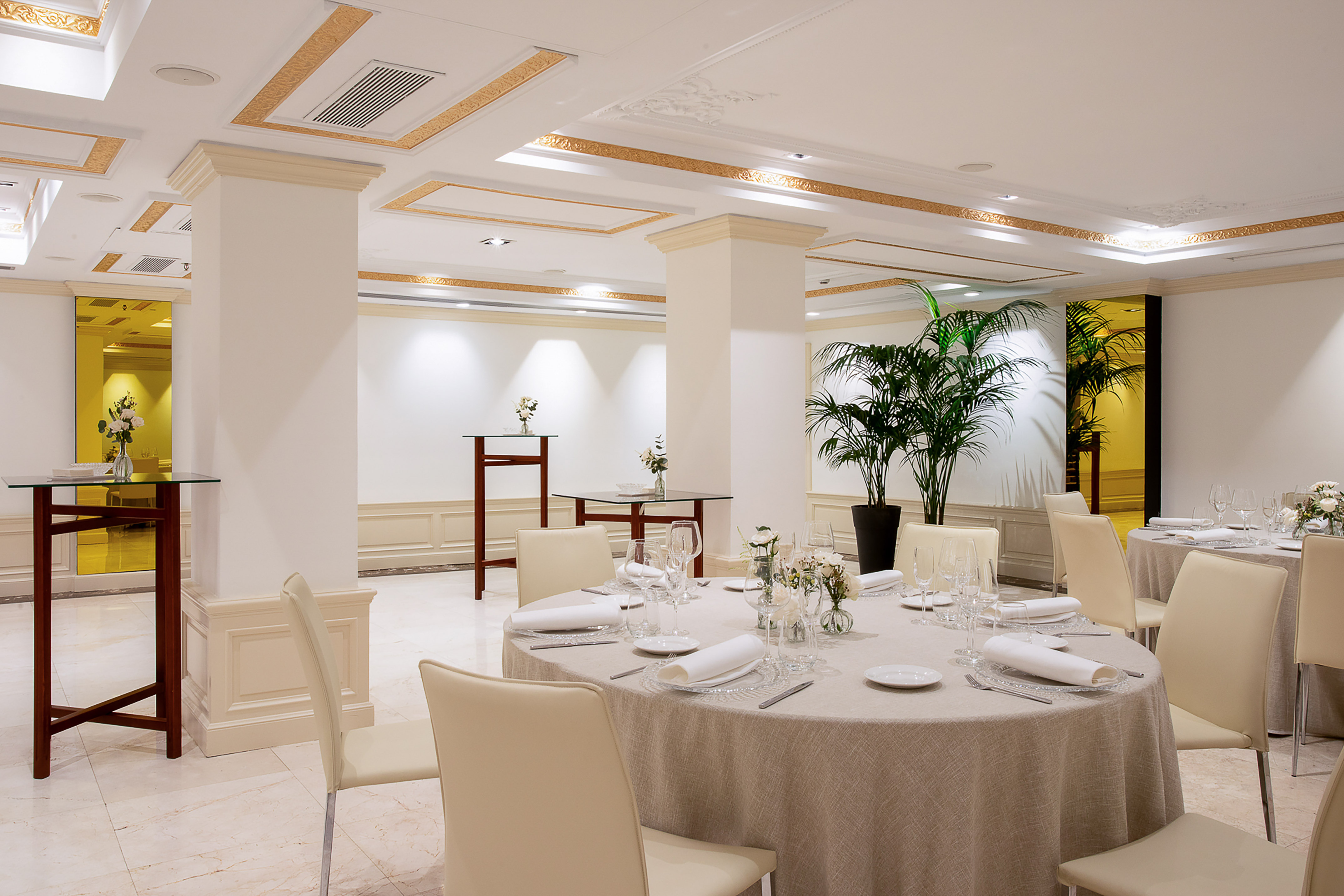 Elegant banquet hall with set round tables, chairs, and gold ceiling accents.
