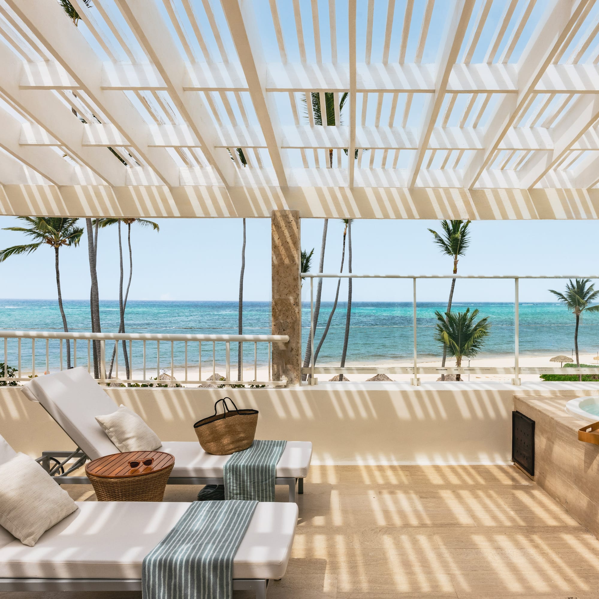 Tropical balcony with ocean view, lounge chairs, jacuzzi, and palm trees.