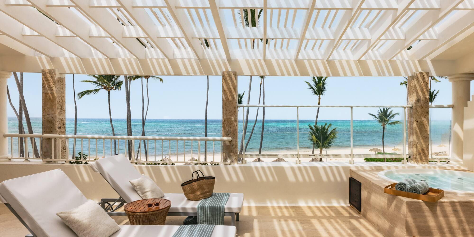 Tropical balcony with ocean view, lounge chairs, jacuzzi, and palm trees.