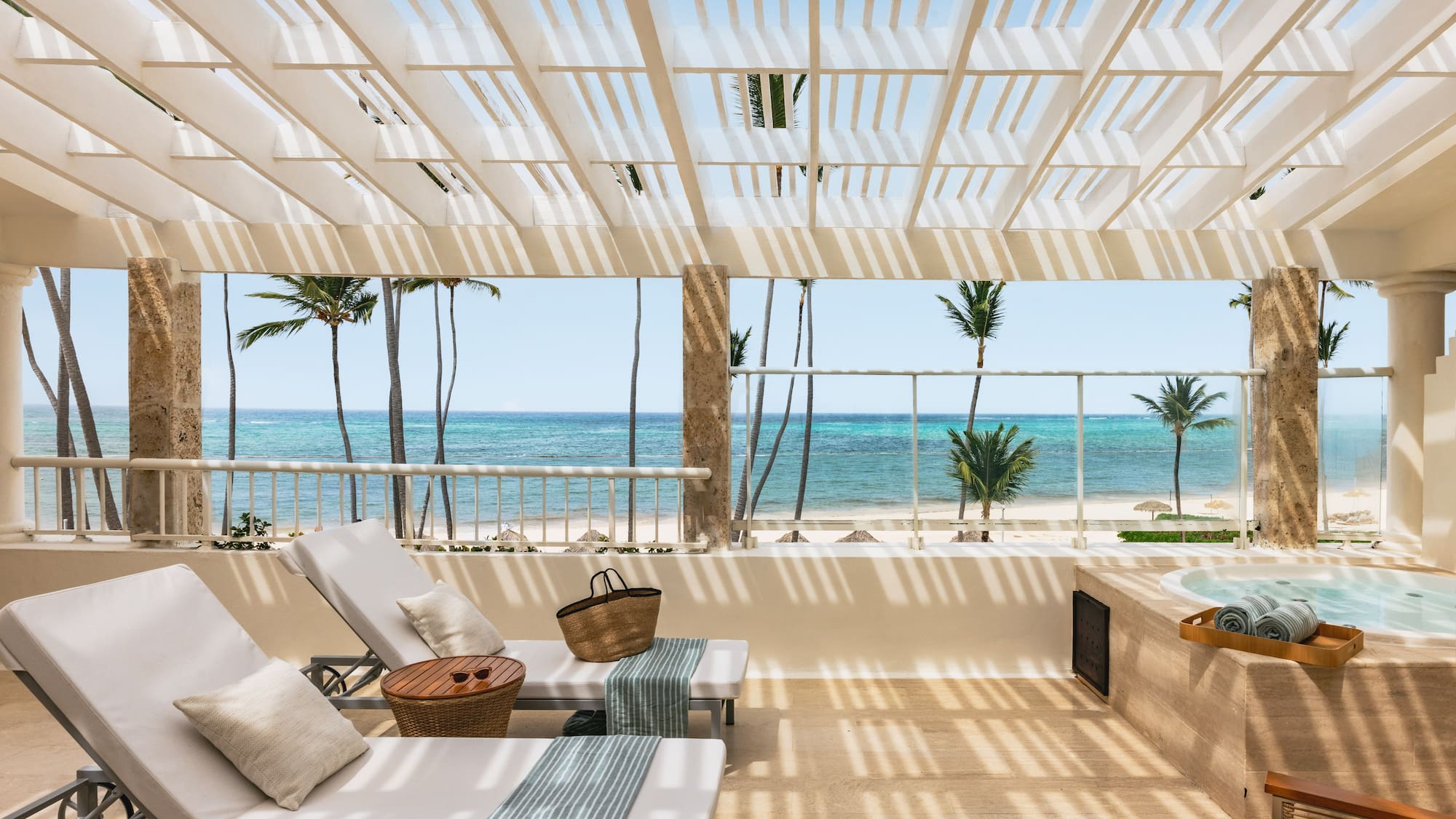 Tropical balcony with ocean view, lounge chairs, jacuzzi, and palm trees.