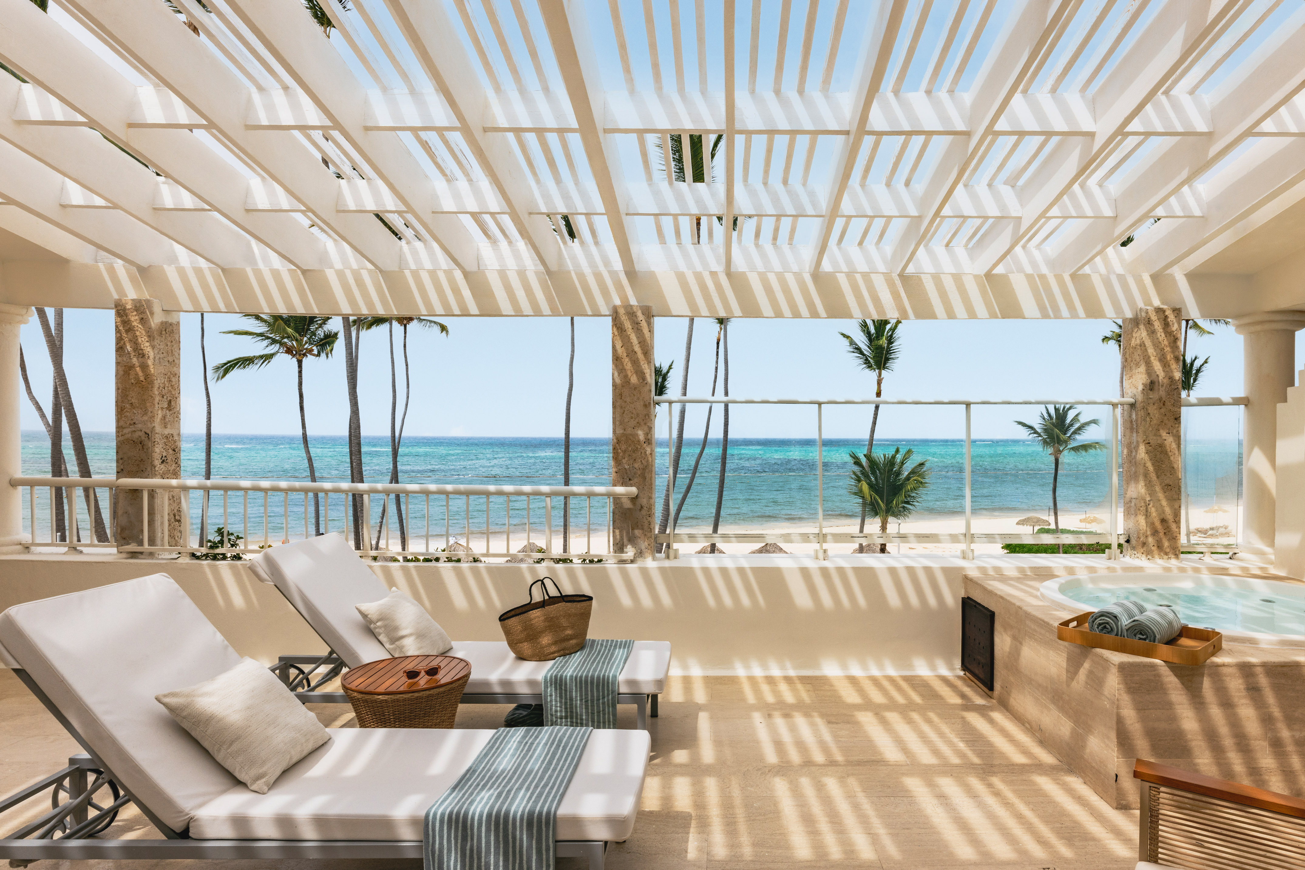 Tropical balcony with ocean view, lounge chairs, jacuzzi, and palm trees.
