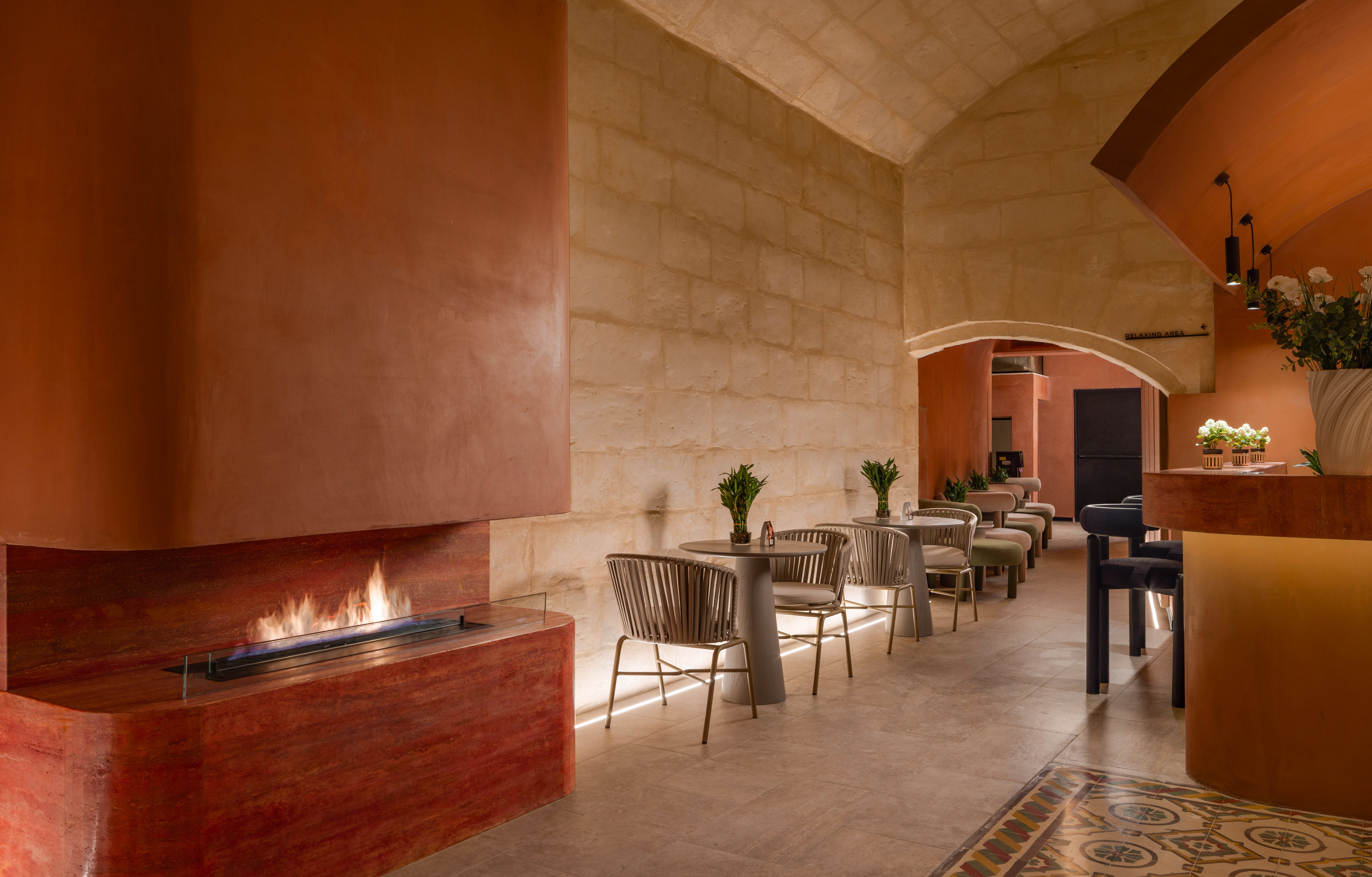 Modern lounge with fireplace, terracotta walls, stone arches, and seating.