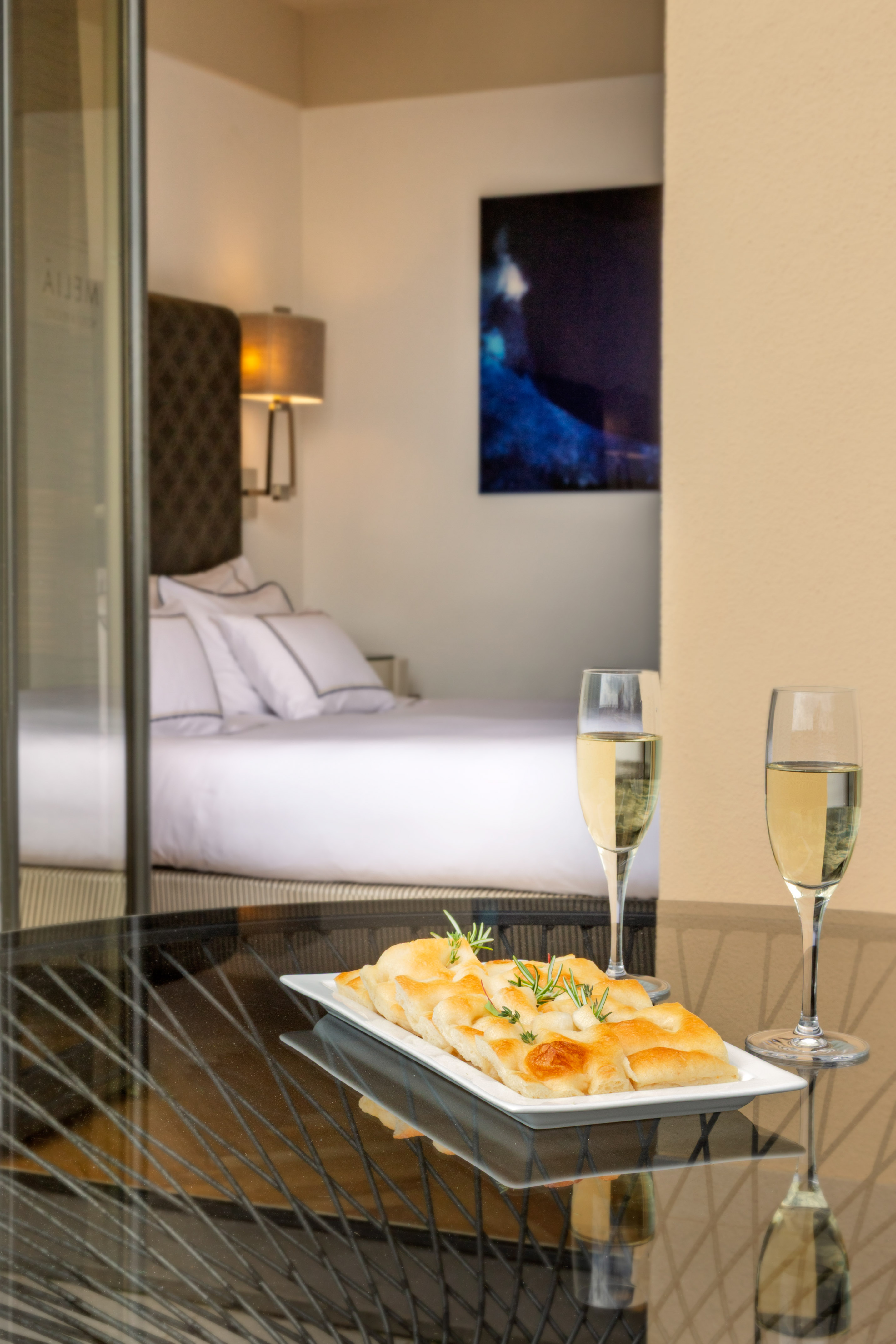 Focaccia and wine on hotel balcony; modern bedroom visible through glass.