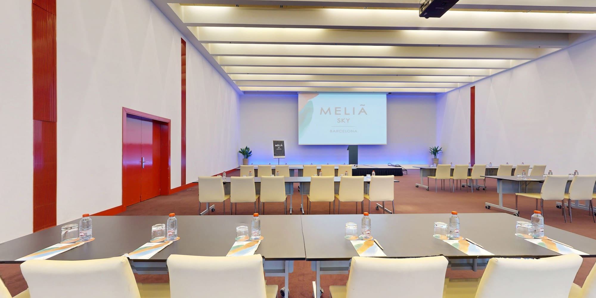 Modern Meliá Sky Barcelona conference room, presentation screen, tables, chairs.