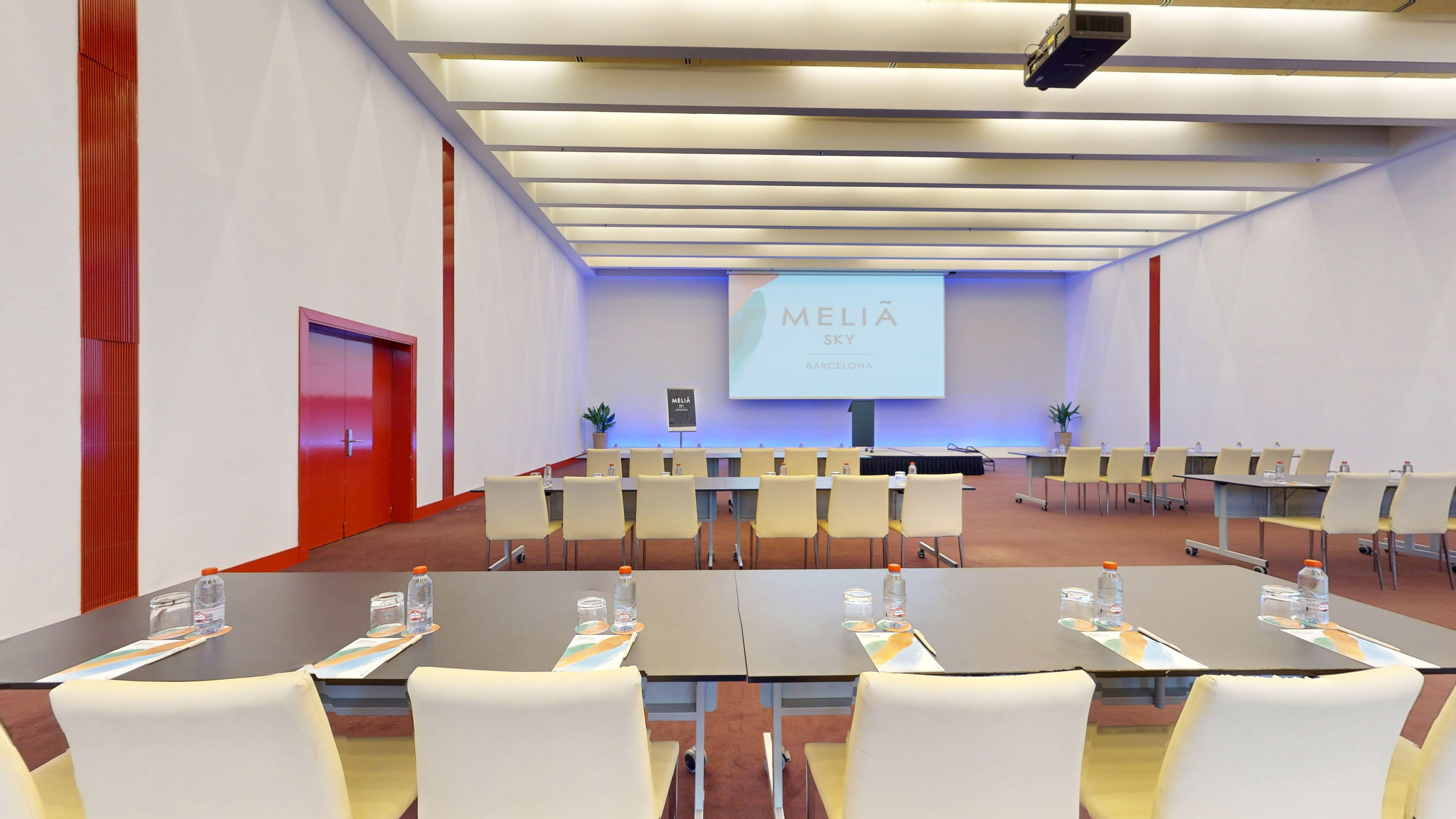 Modern Meliá Sky Barcelona conference room, presentation screen, tables, chairs.