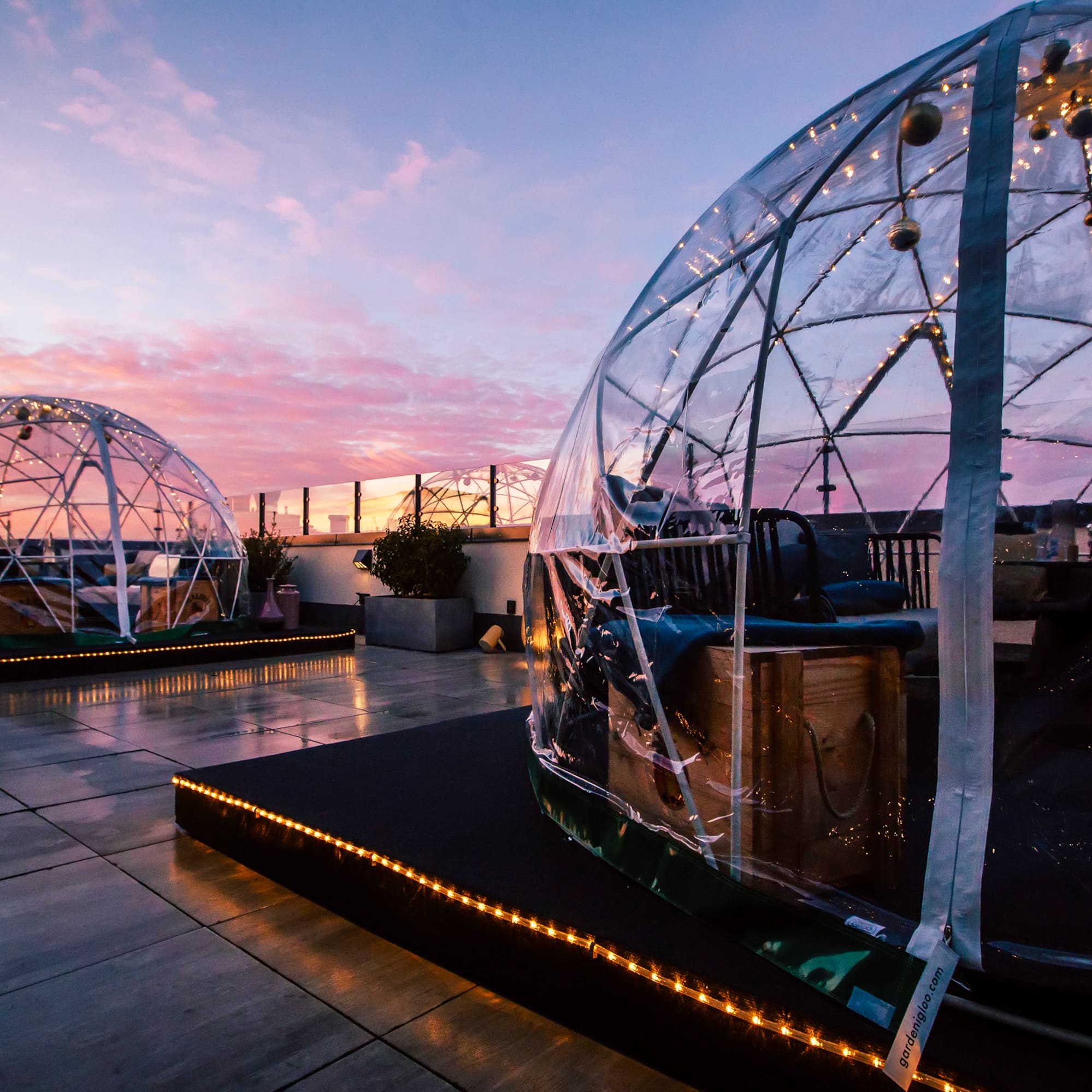 Rooftop lounge with clear dining igloos at sunset, glowing string lights.