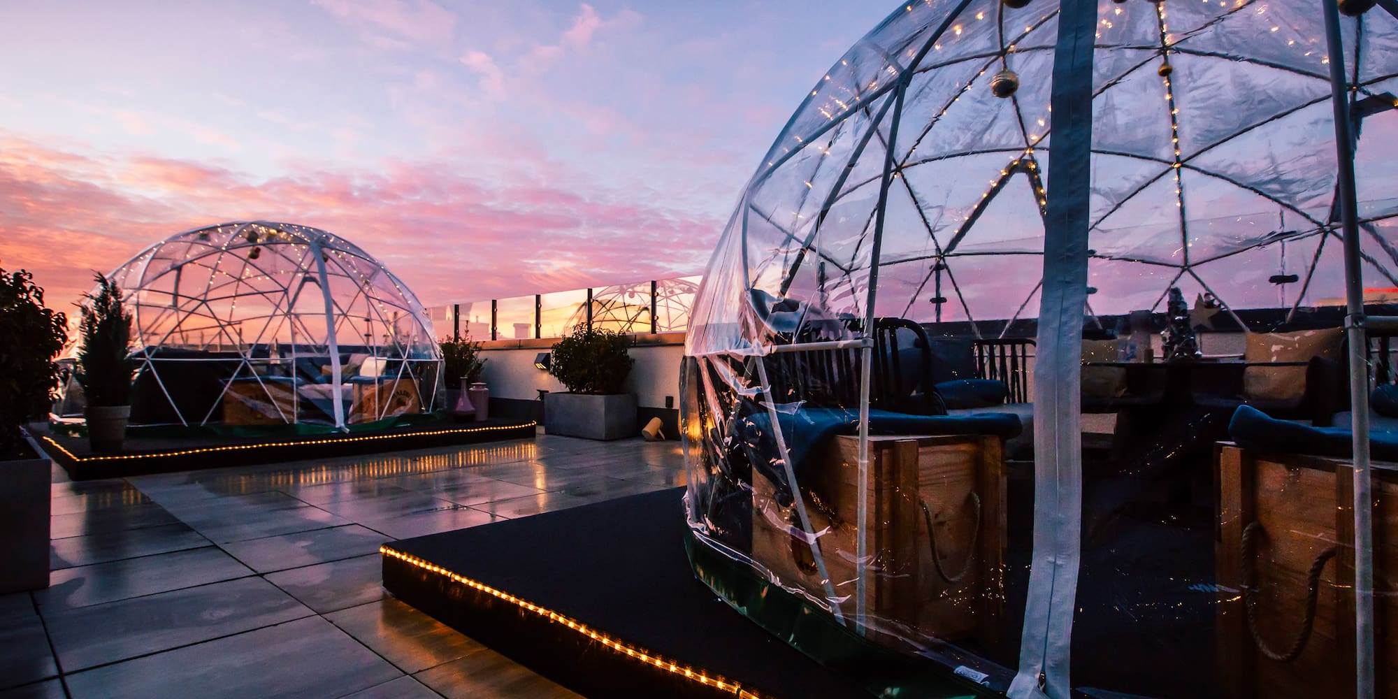 Rooftop lounge with clear dining igloos at sunset, glowing string lights.