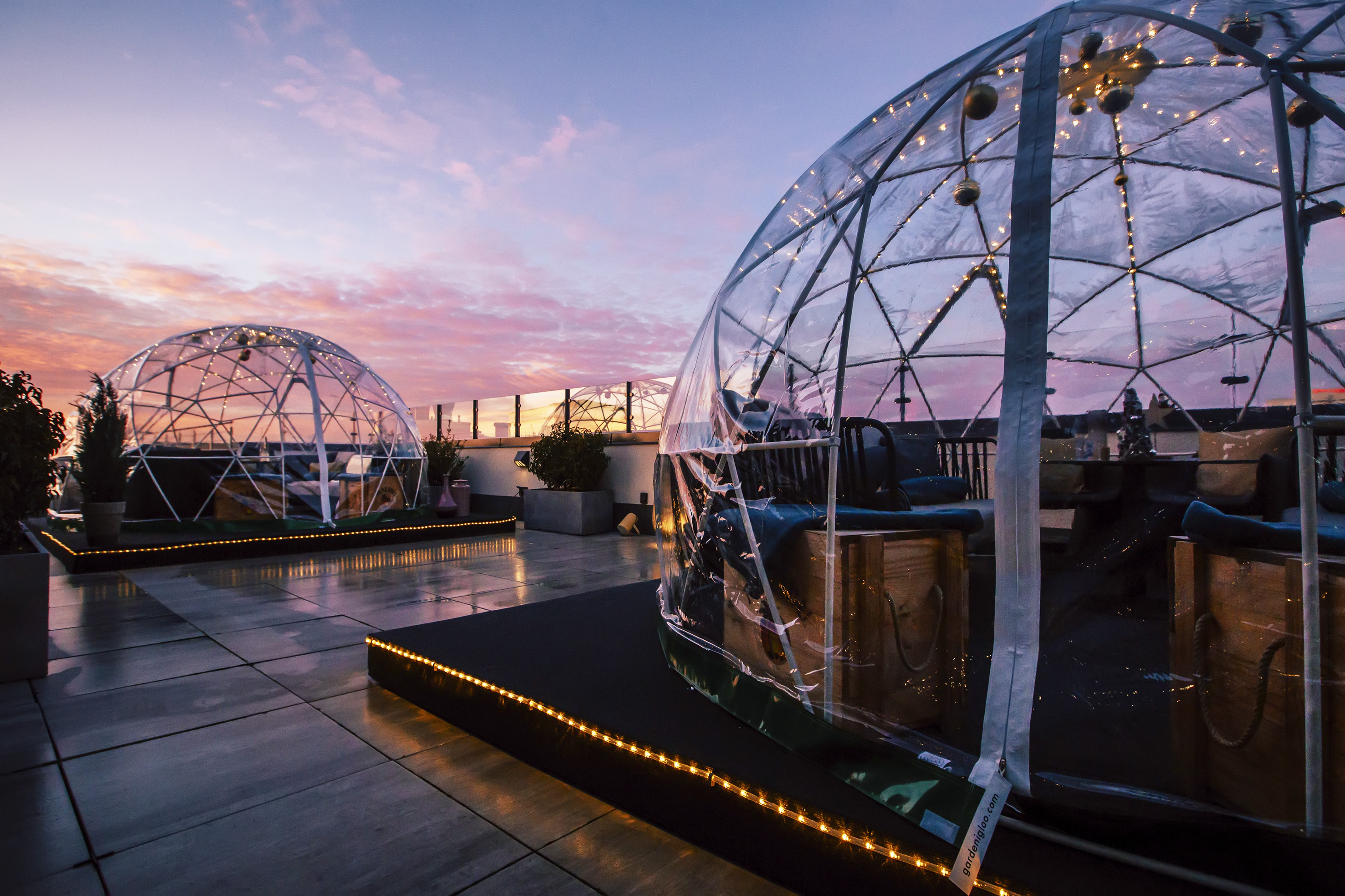 Rooftop lounge with clear dining igloos at sunset, glowing string lights.
