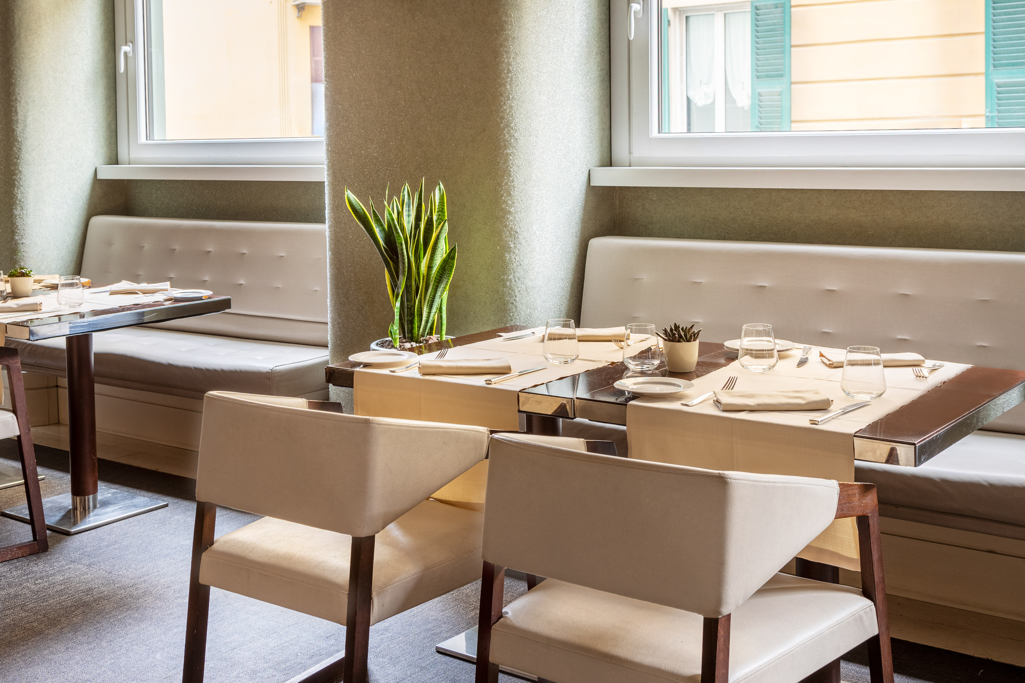 Modern restaurant dining room, set tables, banquette seating, windows.