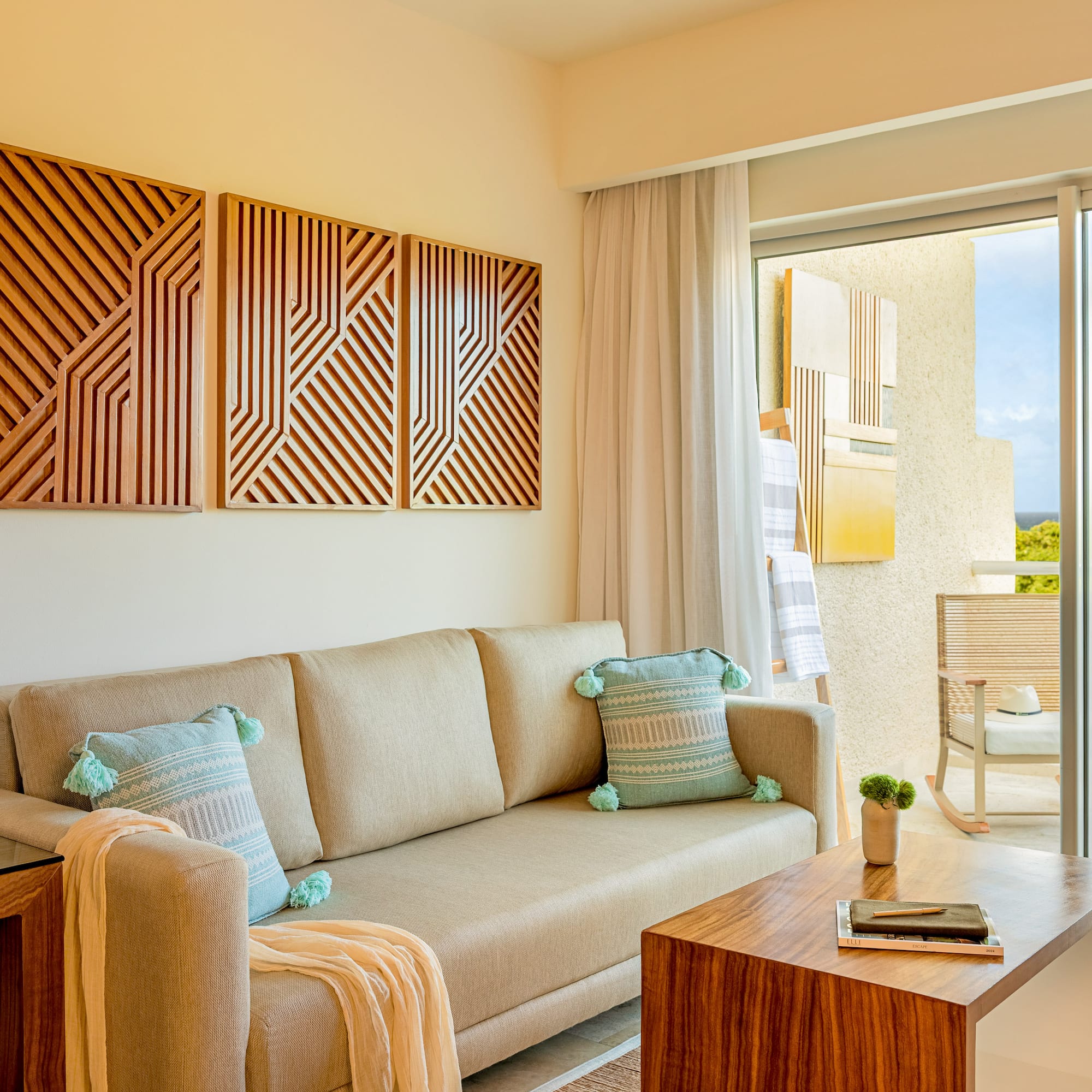 Modern resort living room with sofa, wood art, and balcony view.