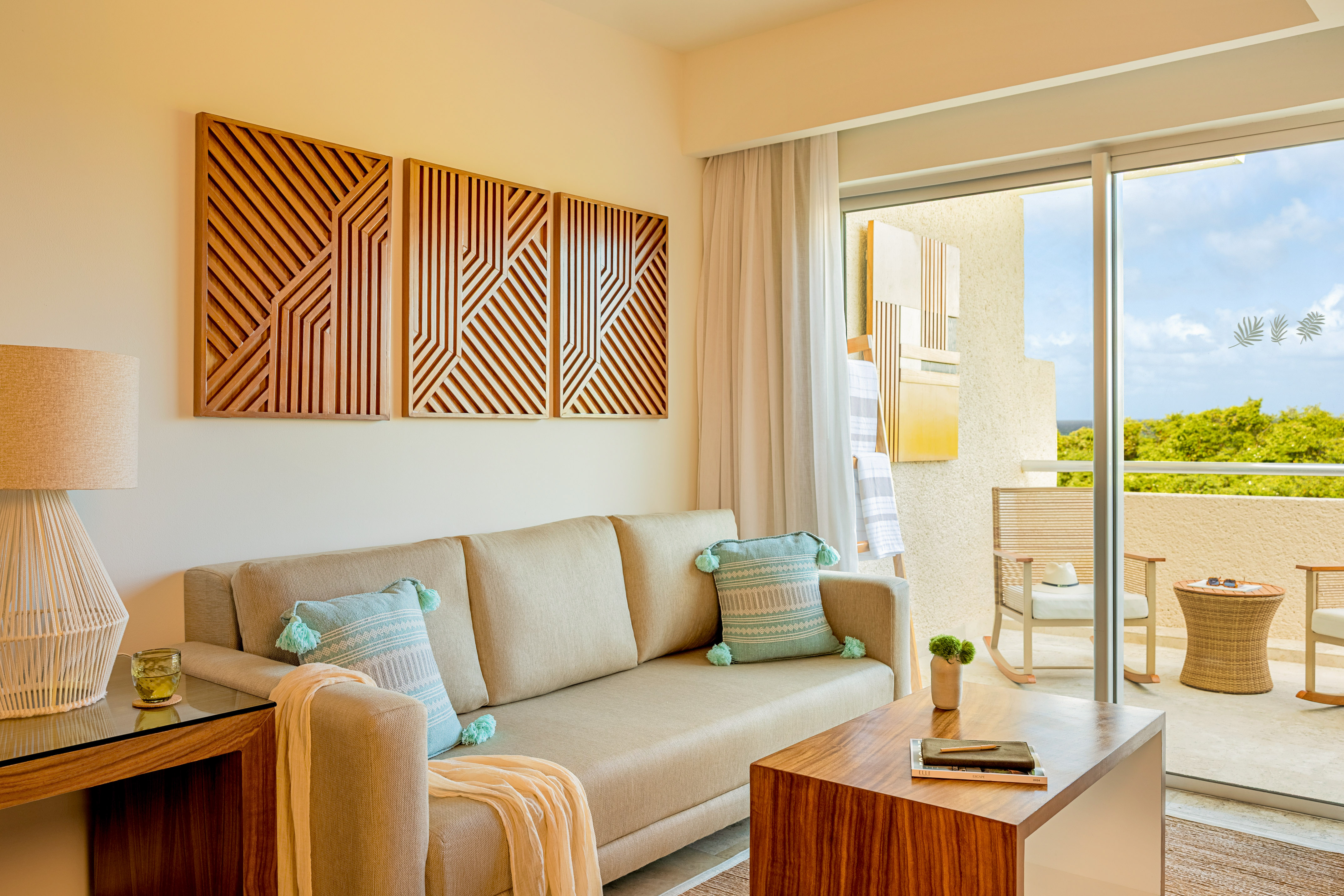 Modern resort living room with sofa, wood art, and balcony view.