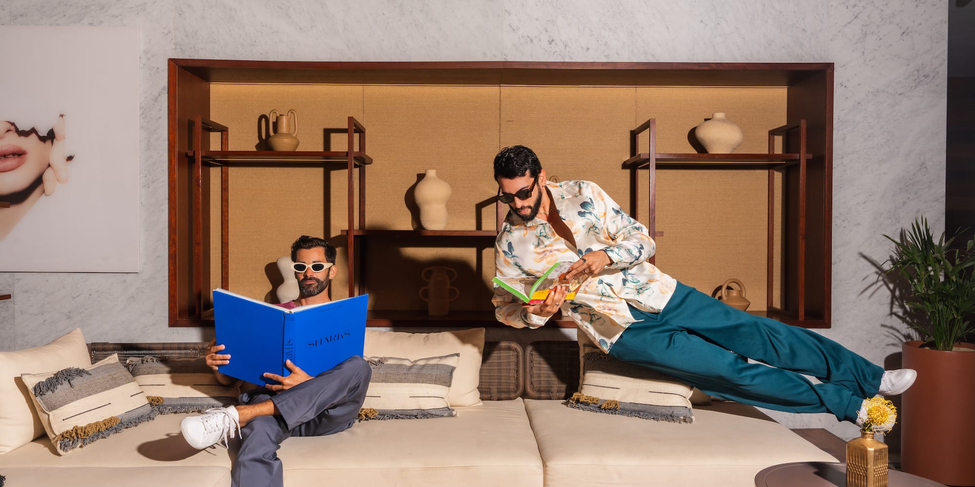 a man in sunglasses flying through the air while another man is reading a book