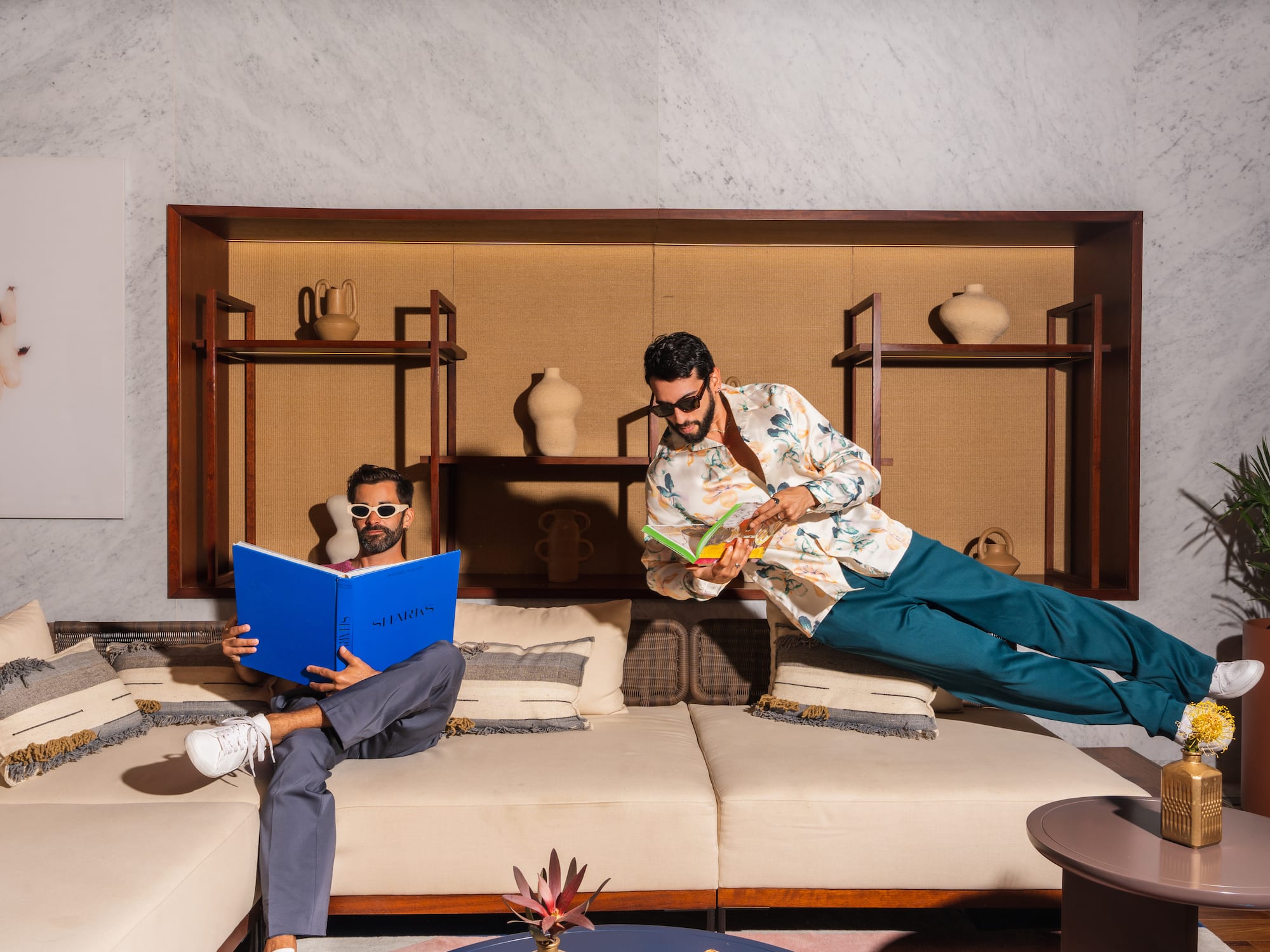 a man in sunglasses flying through the air while another man is reading a book