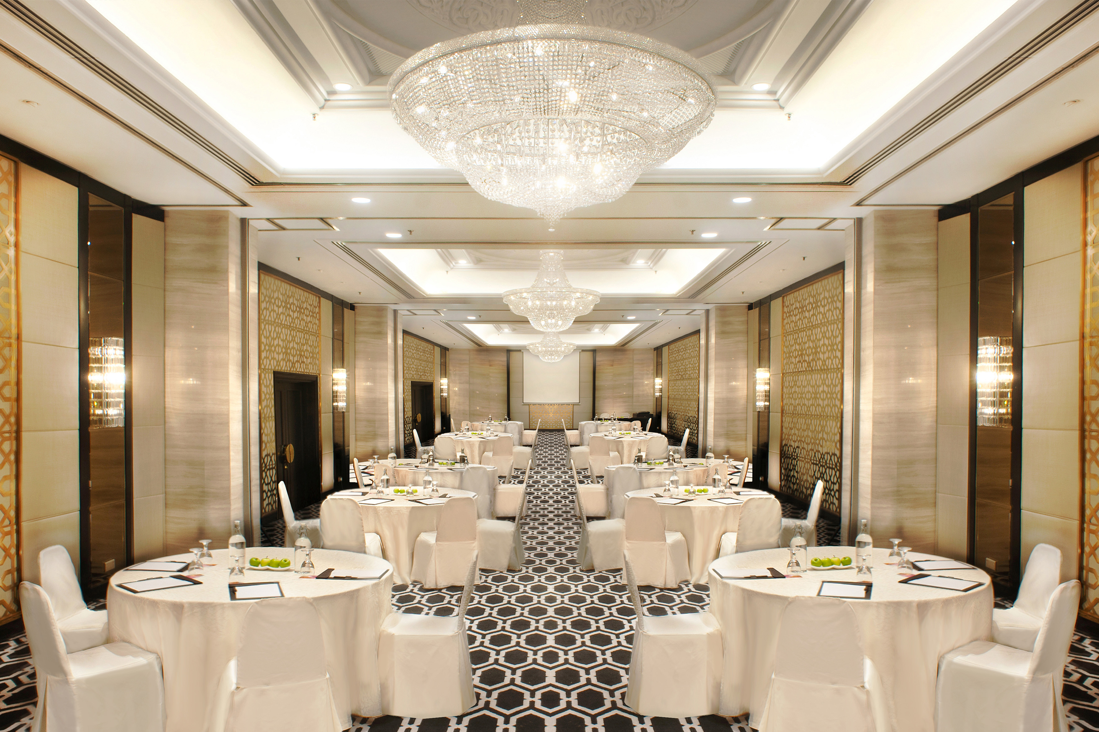 Elegant meeting room setup with round tables, white chairs, and crystal chandeliers.