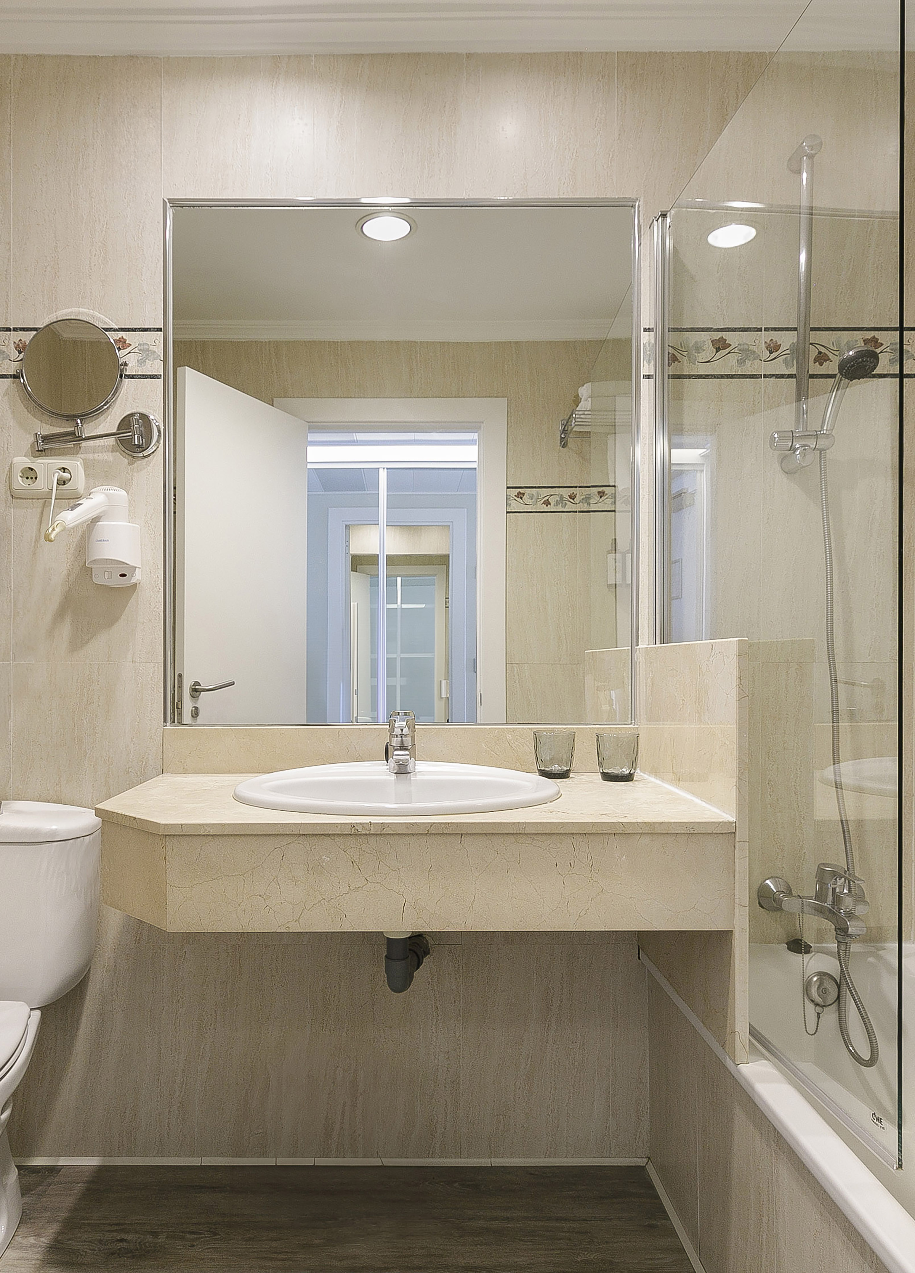 Modern beige tiled bathroom with vanity, sink, toilet, and glass shower enclosure.