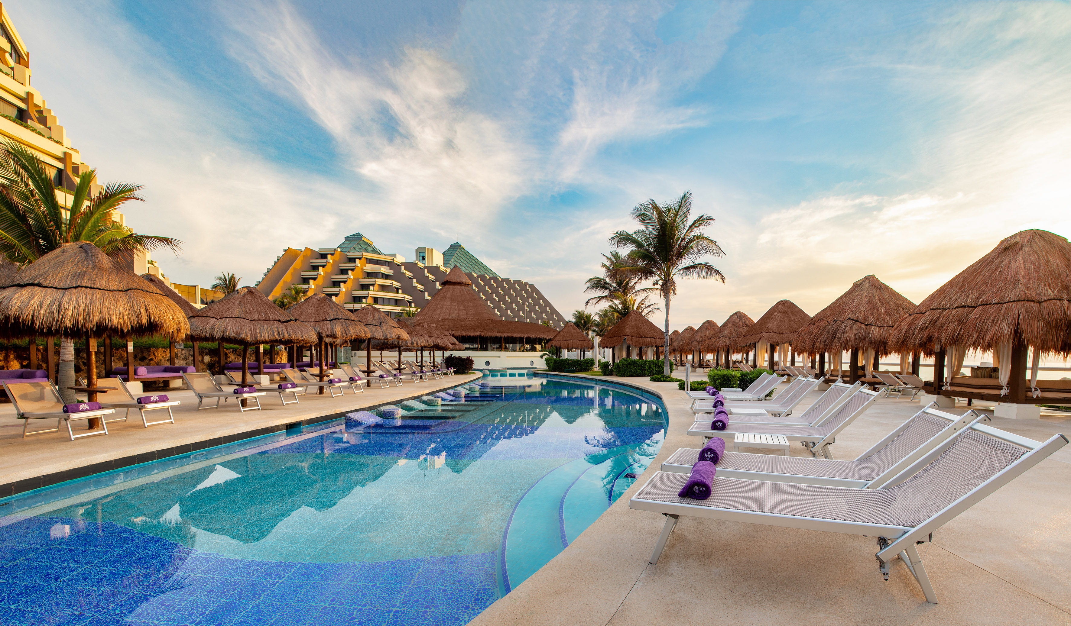 a pool with straw umbrellas and lounge chairs