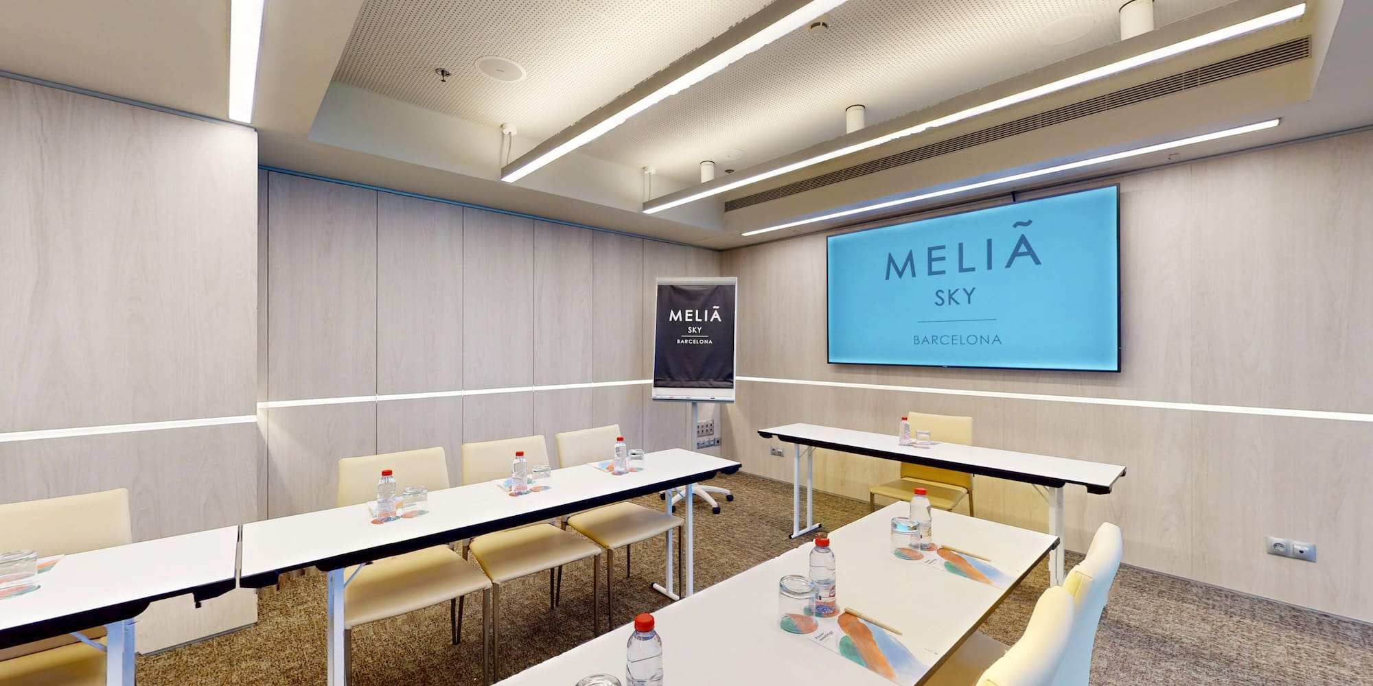 Meliá Sky Barcelona meeting room with tables, chairs, and branded presentation screen.