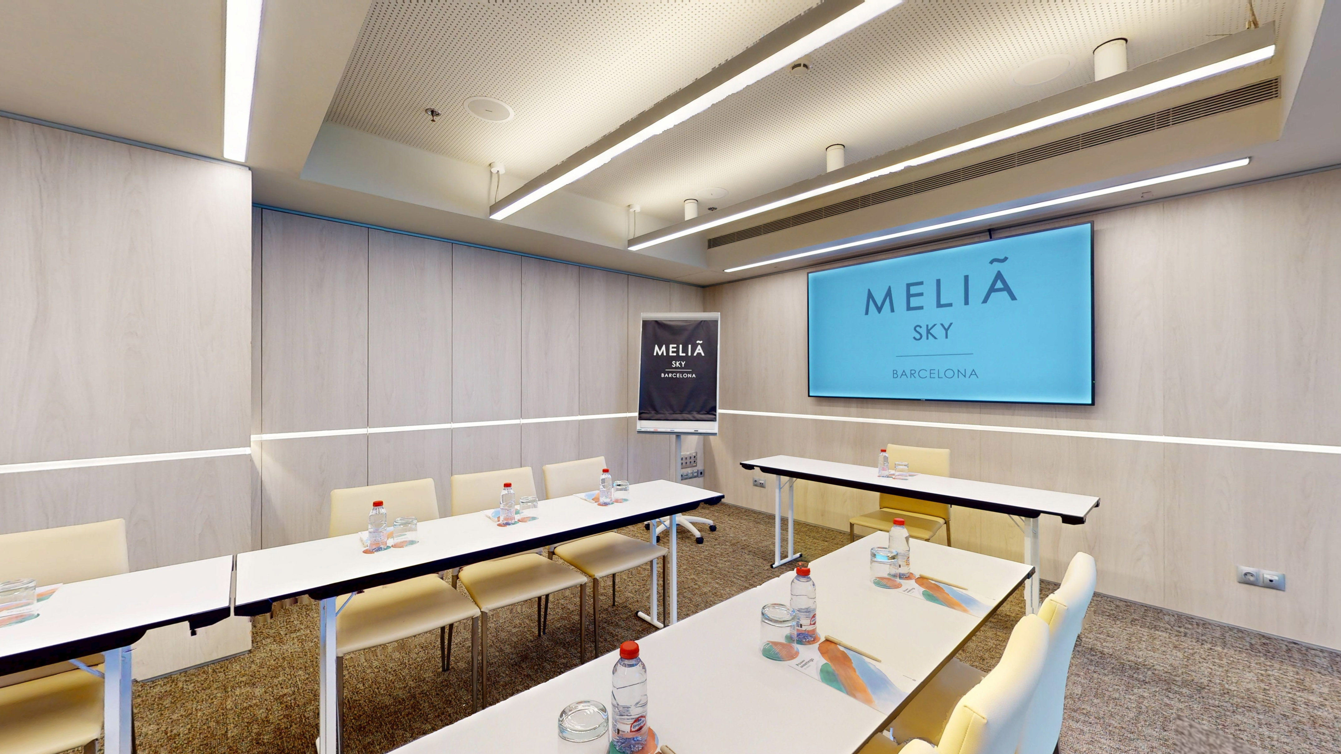 Meliá Sky Barcelona meeting room with tables, chairs, and branded presentation screen.