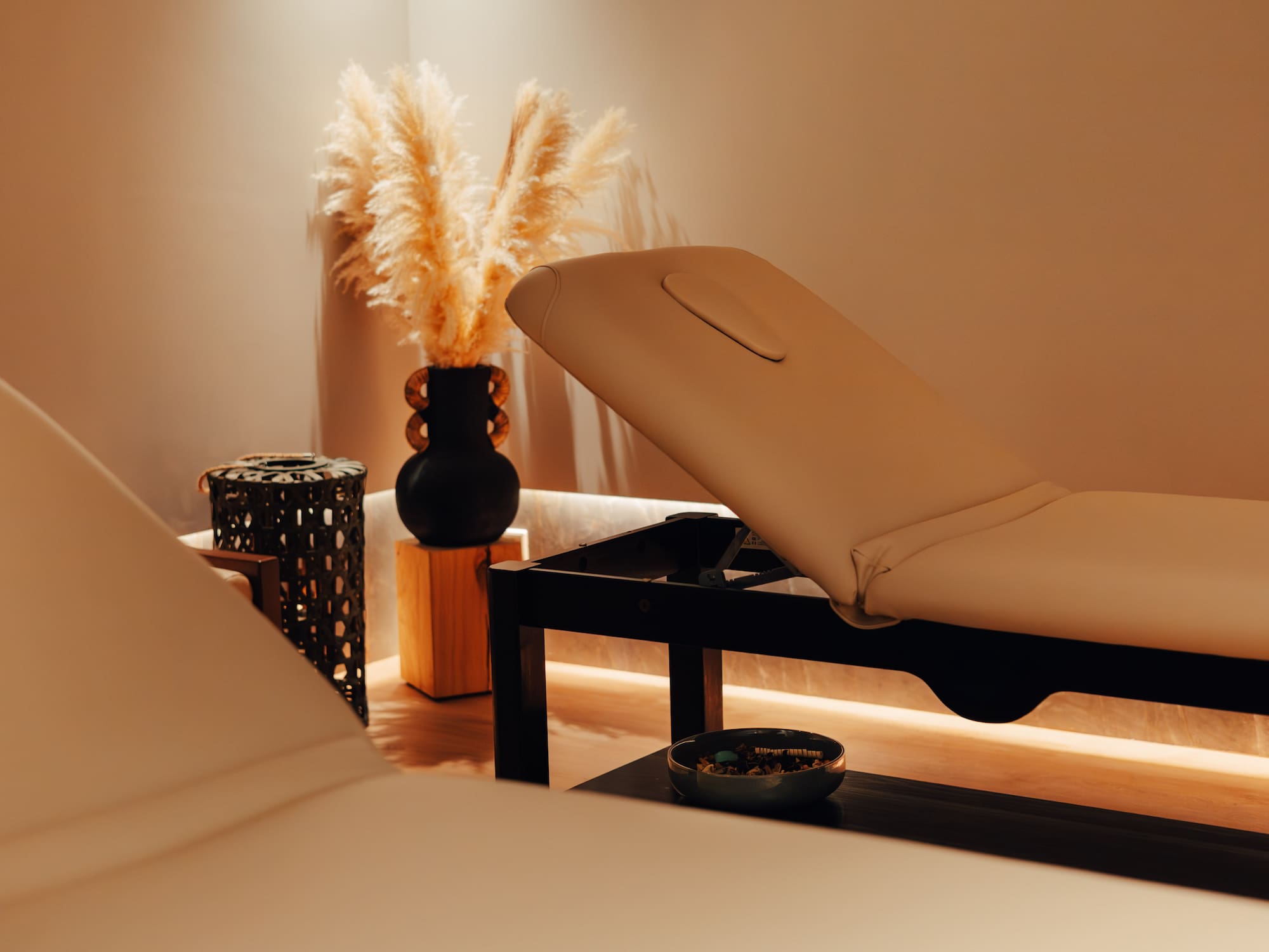 Warm spa treatment room with two beige massage beds and pampas grass decor.
