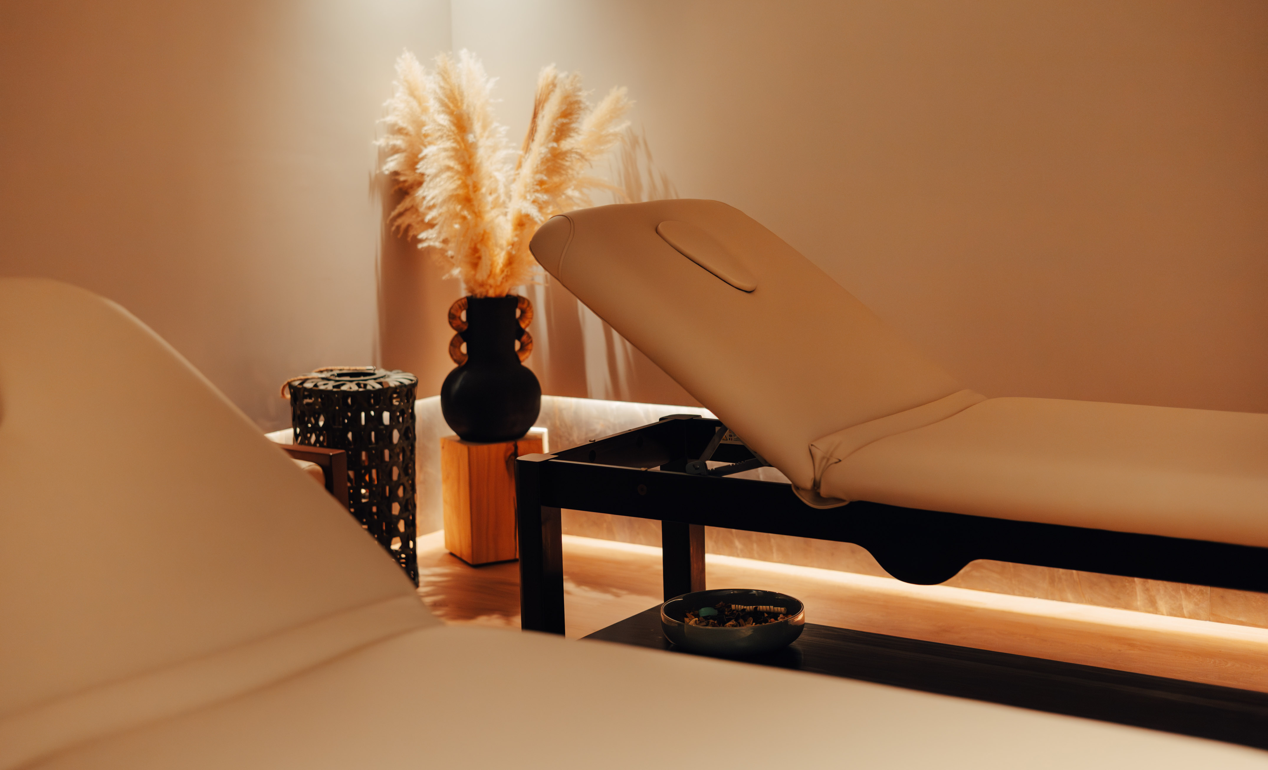 Serene spa treatment room with two massage tables, pampas grass decor, soft lighting.