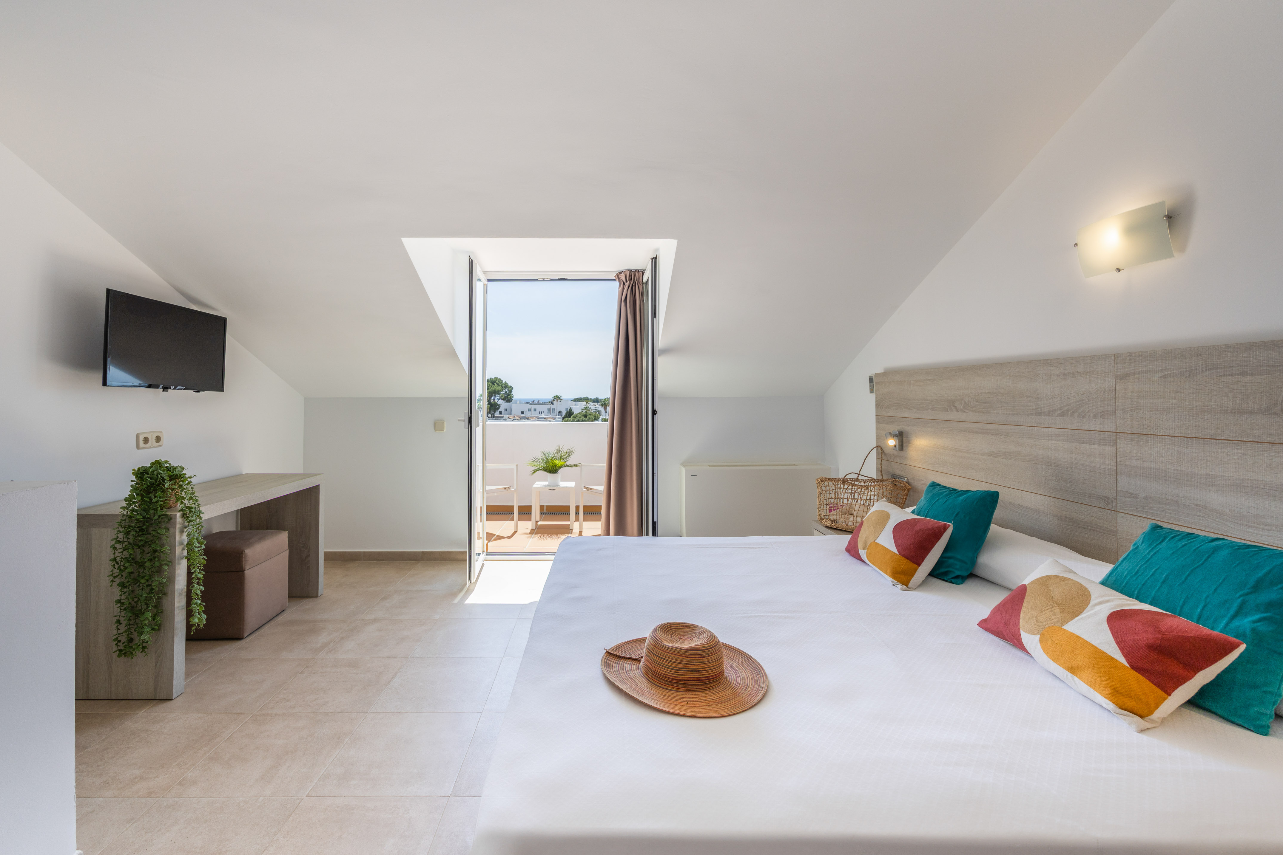 Loft bedroom with private balcony, king-size bed, colorful pillows, and TV.