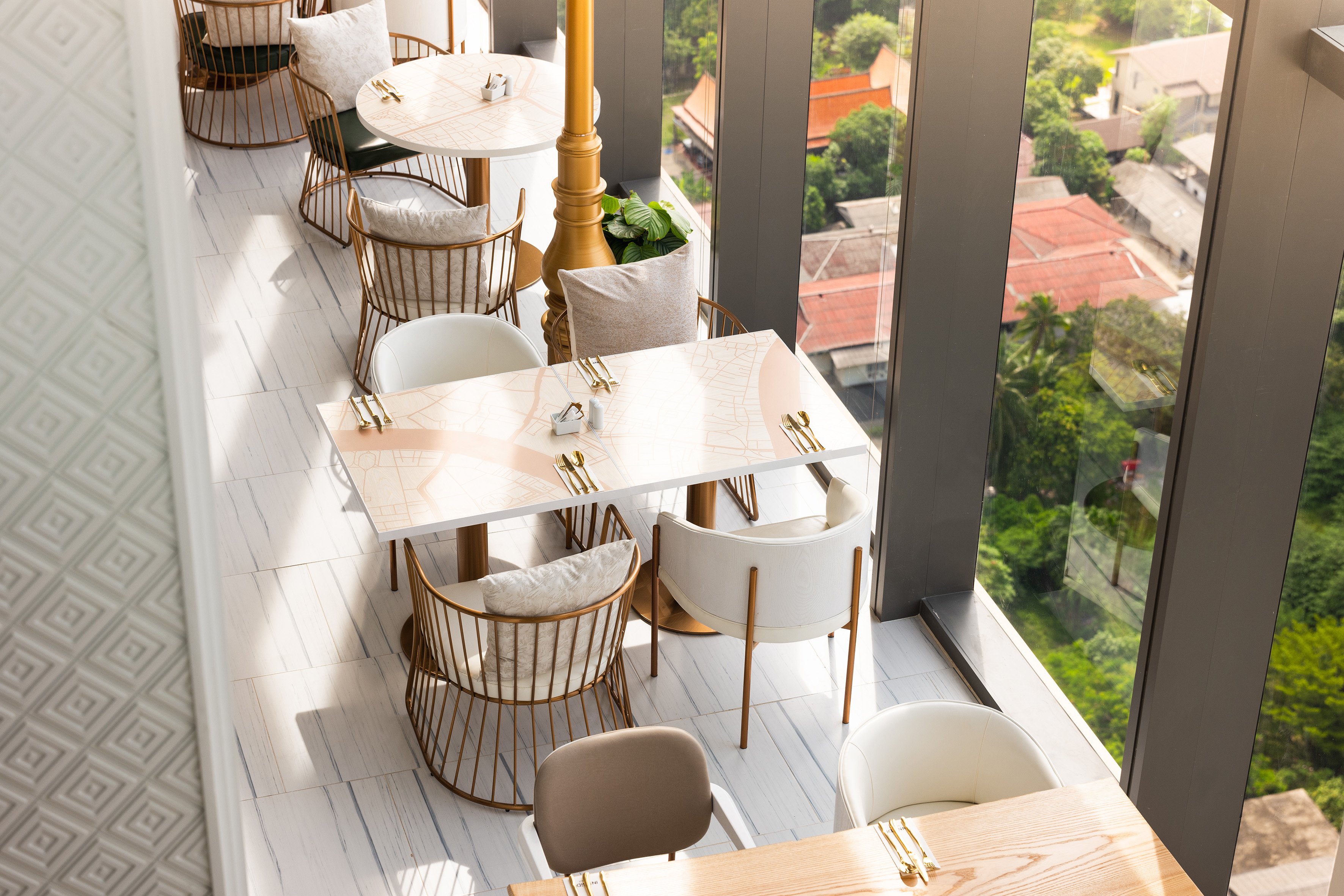 Elegant restaurant interior with city view, map tables, and modern gold chairs.