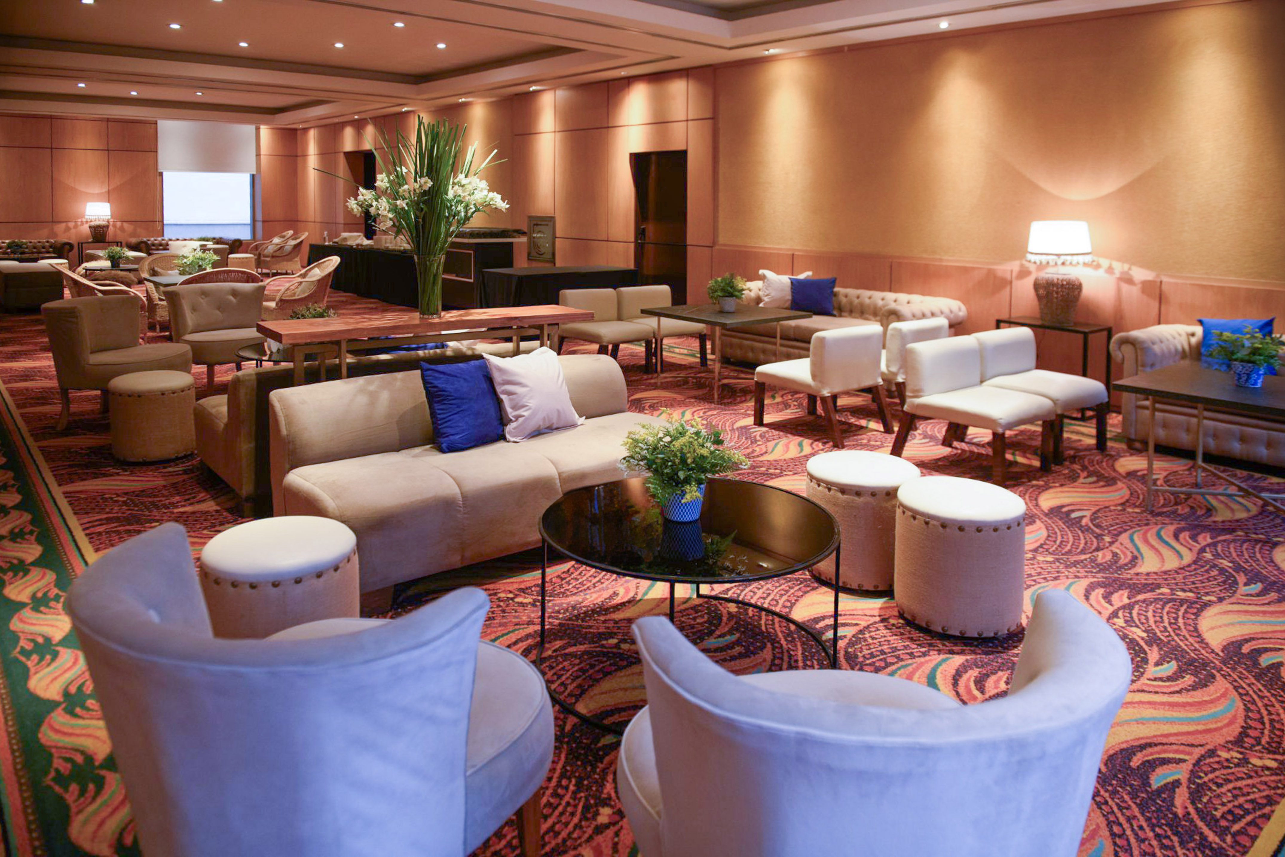 Hotel lounge with beige seating, coffee tables, and colorful patterned carpet.