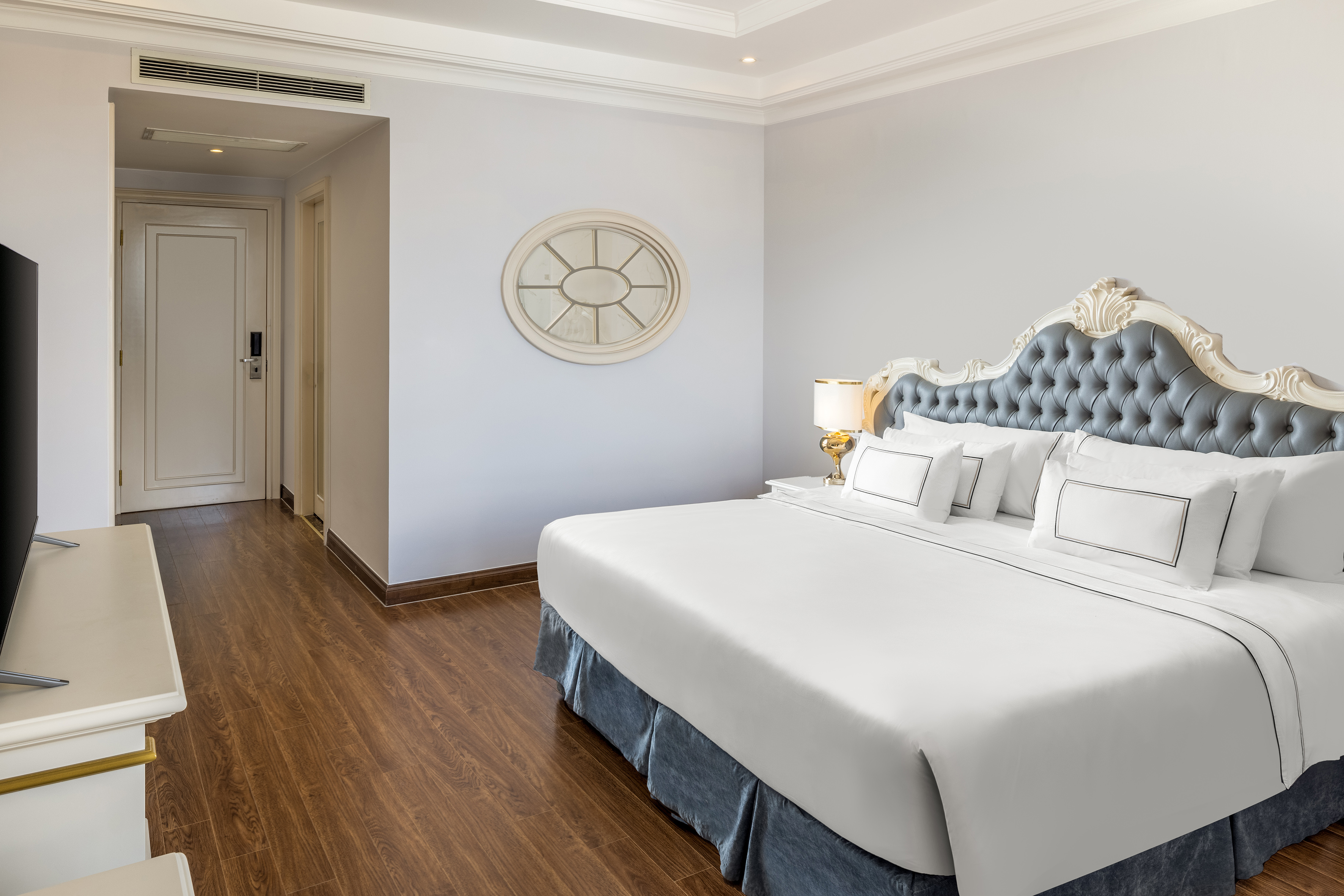 Luxury hotel room with king bed, blue tufted headboard, and wood floor.