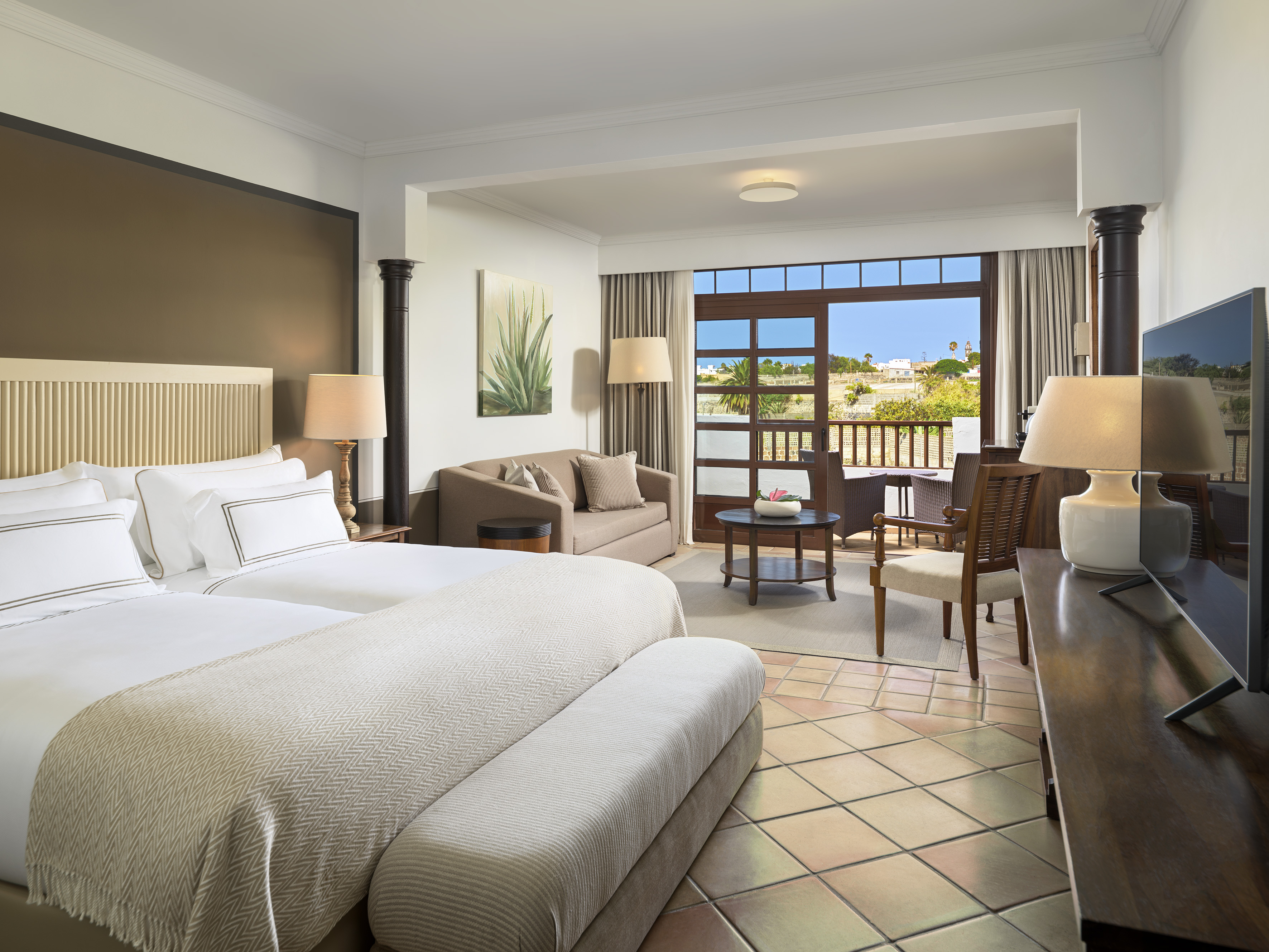 Bright hotel suite with twin beds, living area, and sunny balcony.