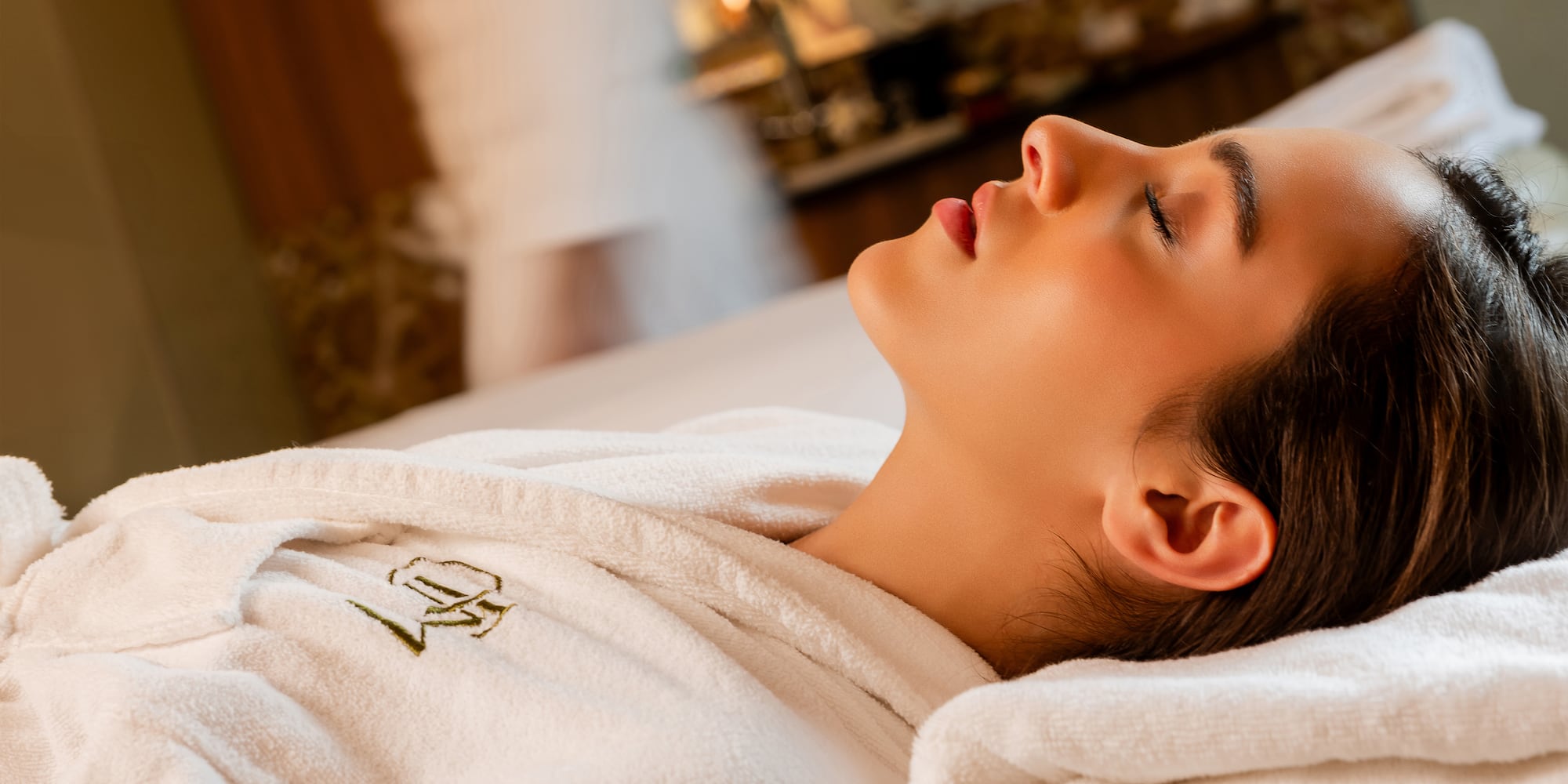 Serene woman with closed eyes in a plush white bathrobe at a luxury spa.