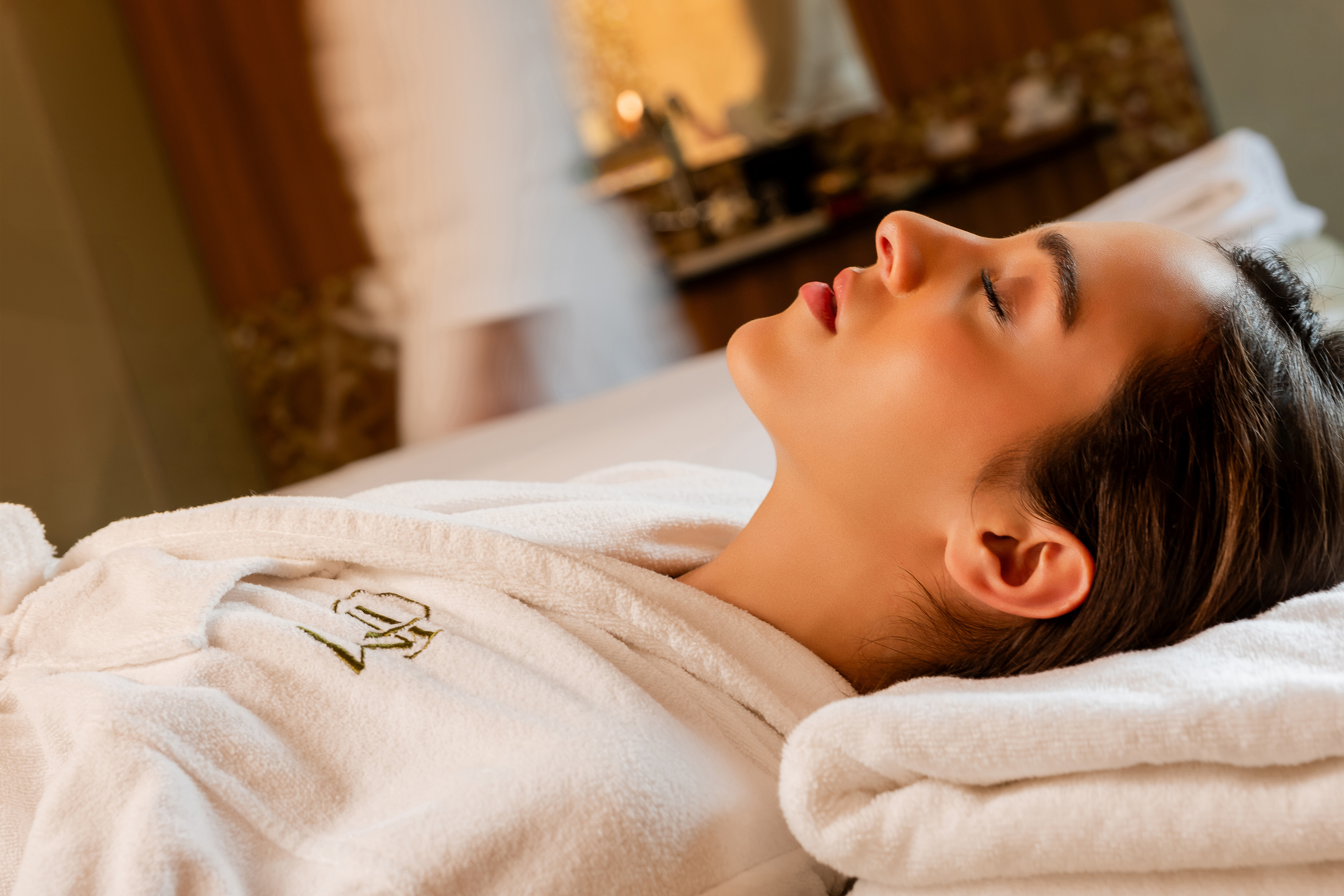 Serene woman with closed eyes in a plush white bathrobe at a luxury spa.