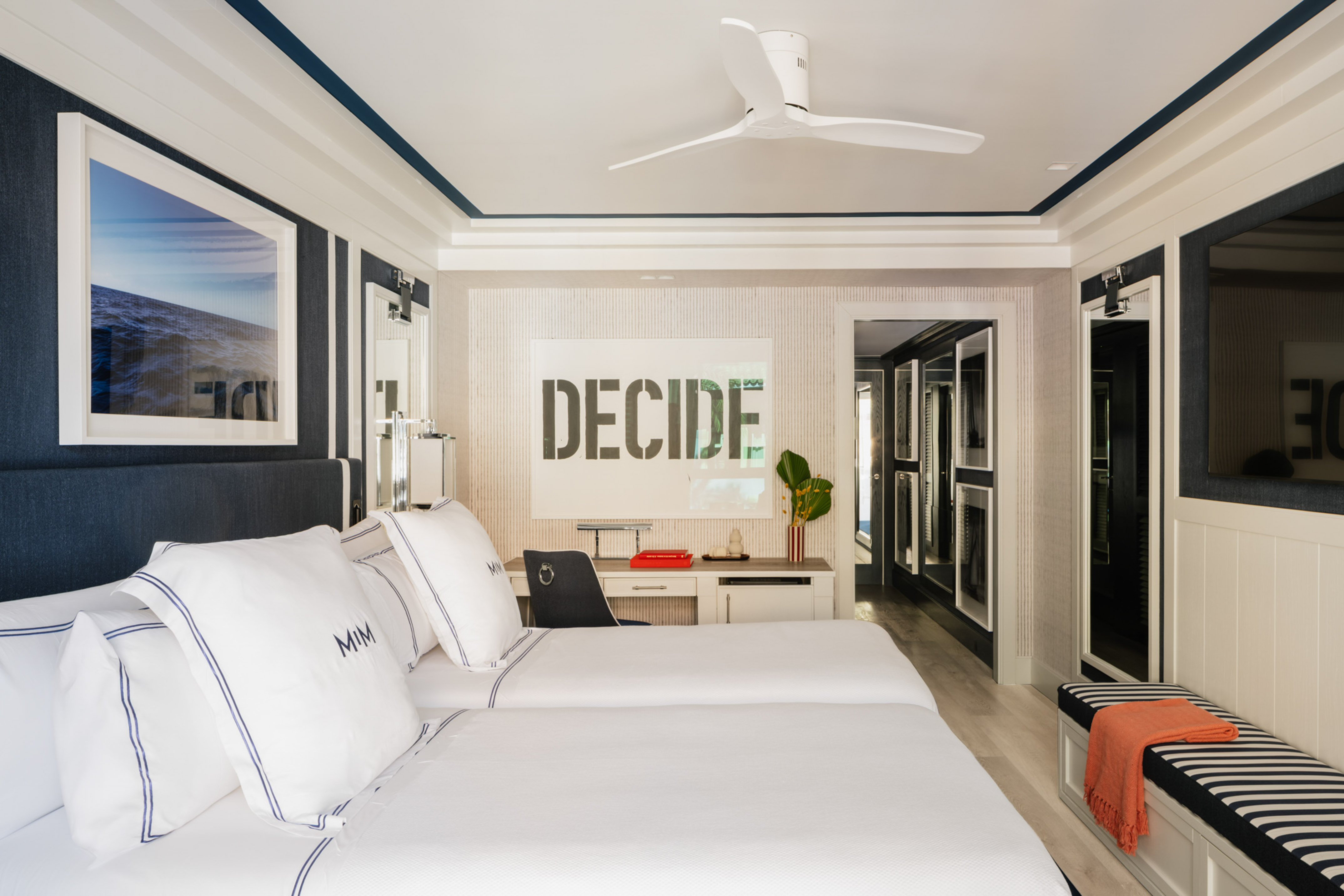 Modern nautical twin bedroom with blue and white decor, ocean art, and desk.