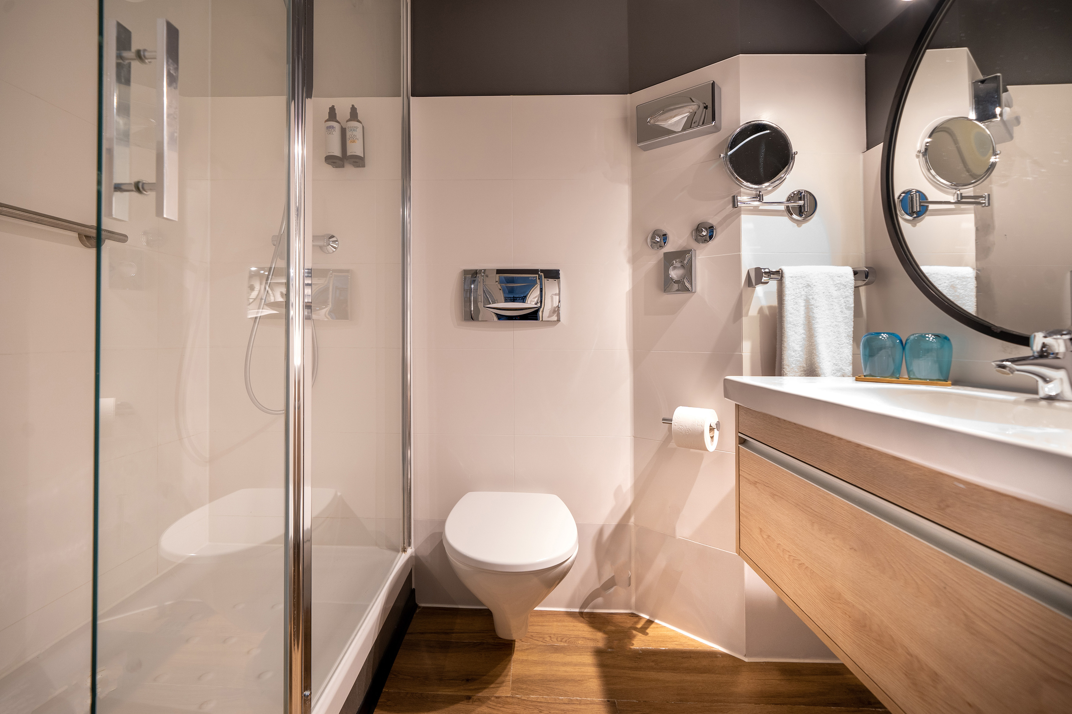 Modern hotel bathroom with glass shower, toilet, and wood vanity sink.