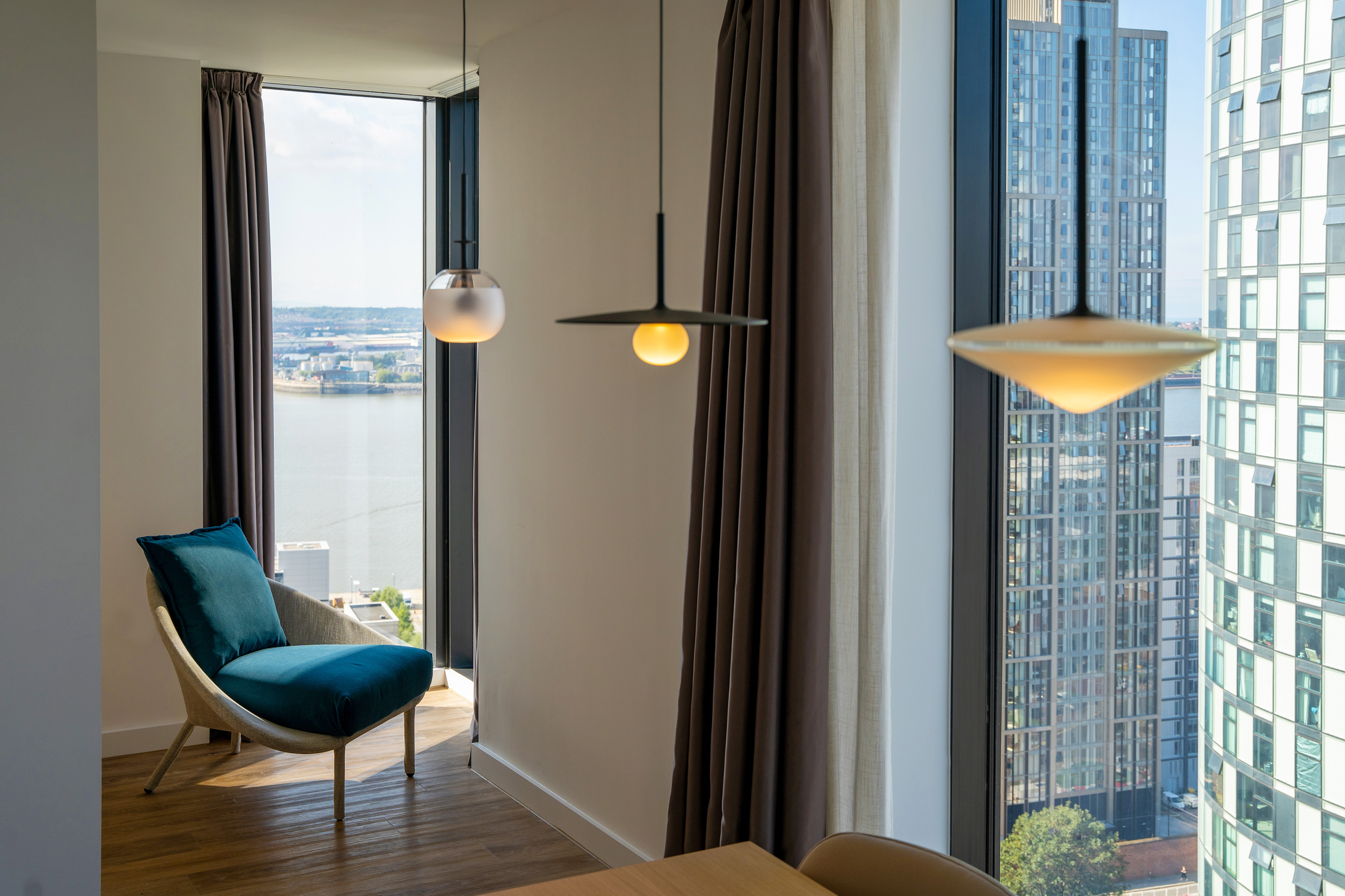 Modern apartment with blue armchair, pendant lights, and city skyline view.