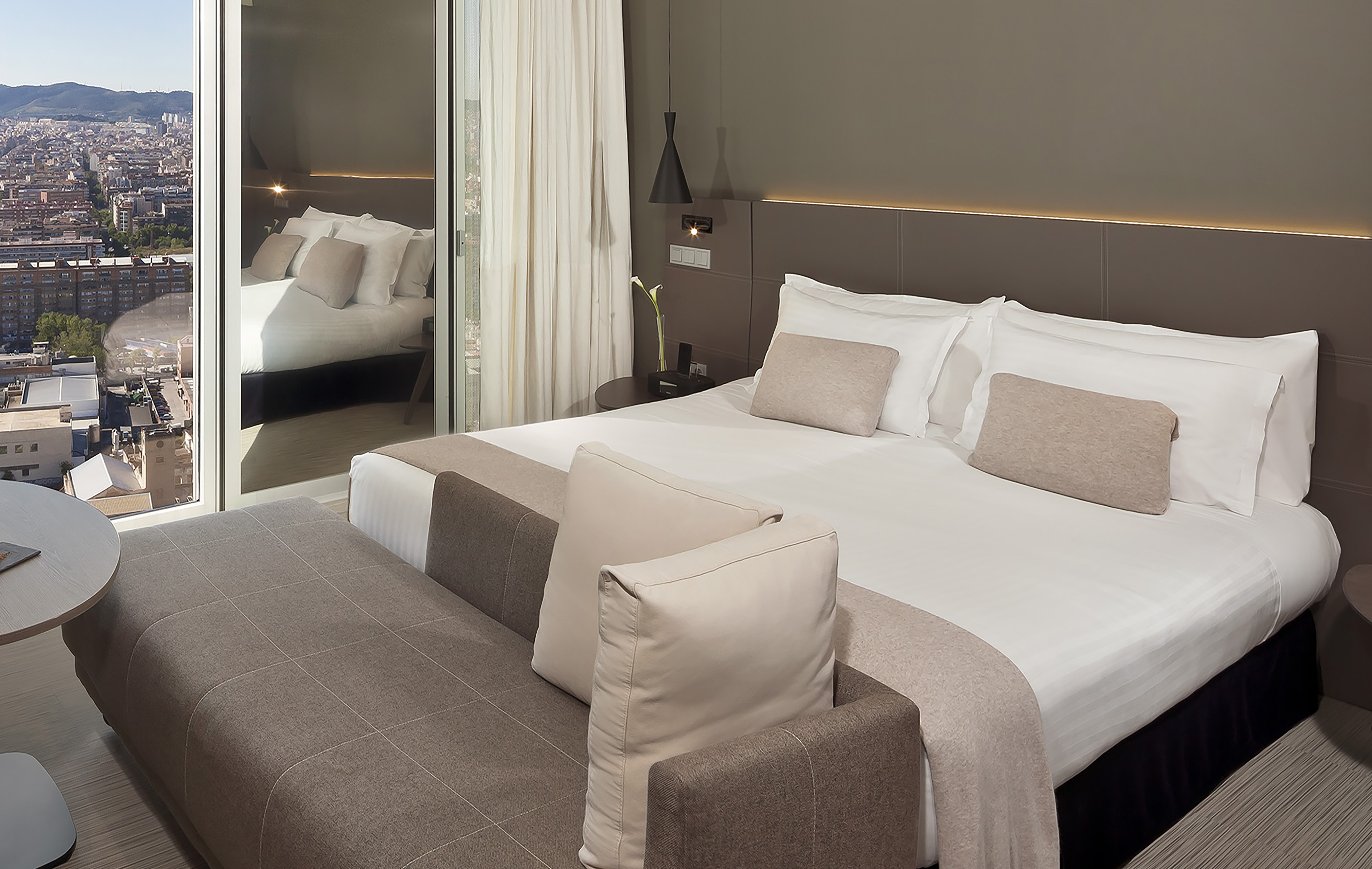 Modern hotel room with large bed, neutral decor, and city view.